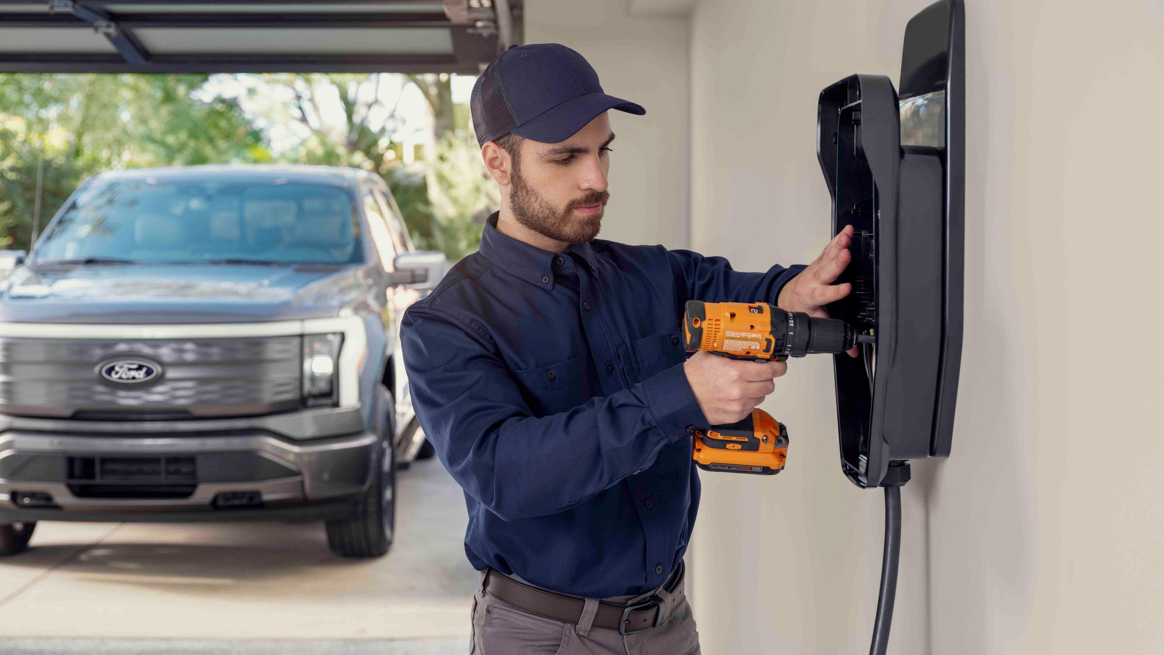 A man installing a home charging station in a garage, with a 2025 Ford F-150® Lightning® pickup parked outside the door