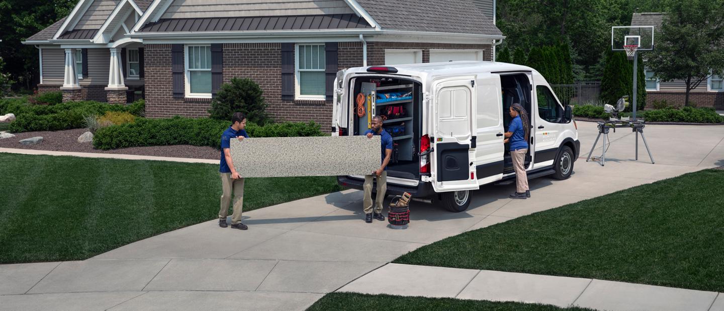 Two workers unloading a length of big, heavy granite from a 2025 Ford Transit® van