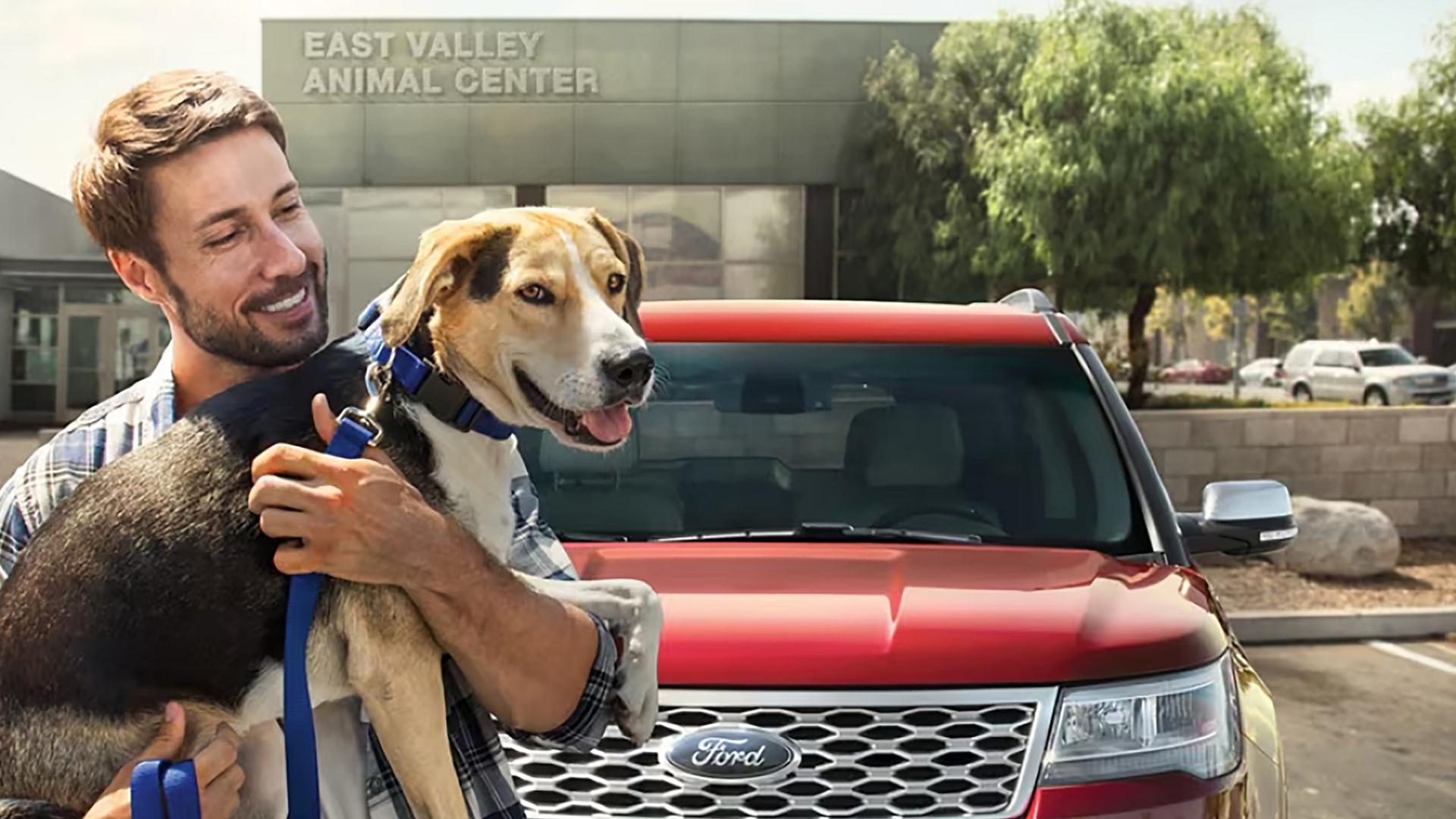 An owner holds their dog in front of their Ford vehicle