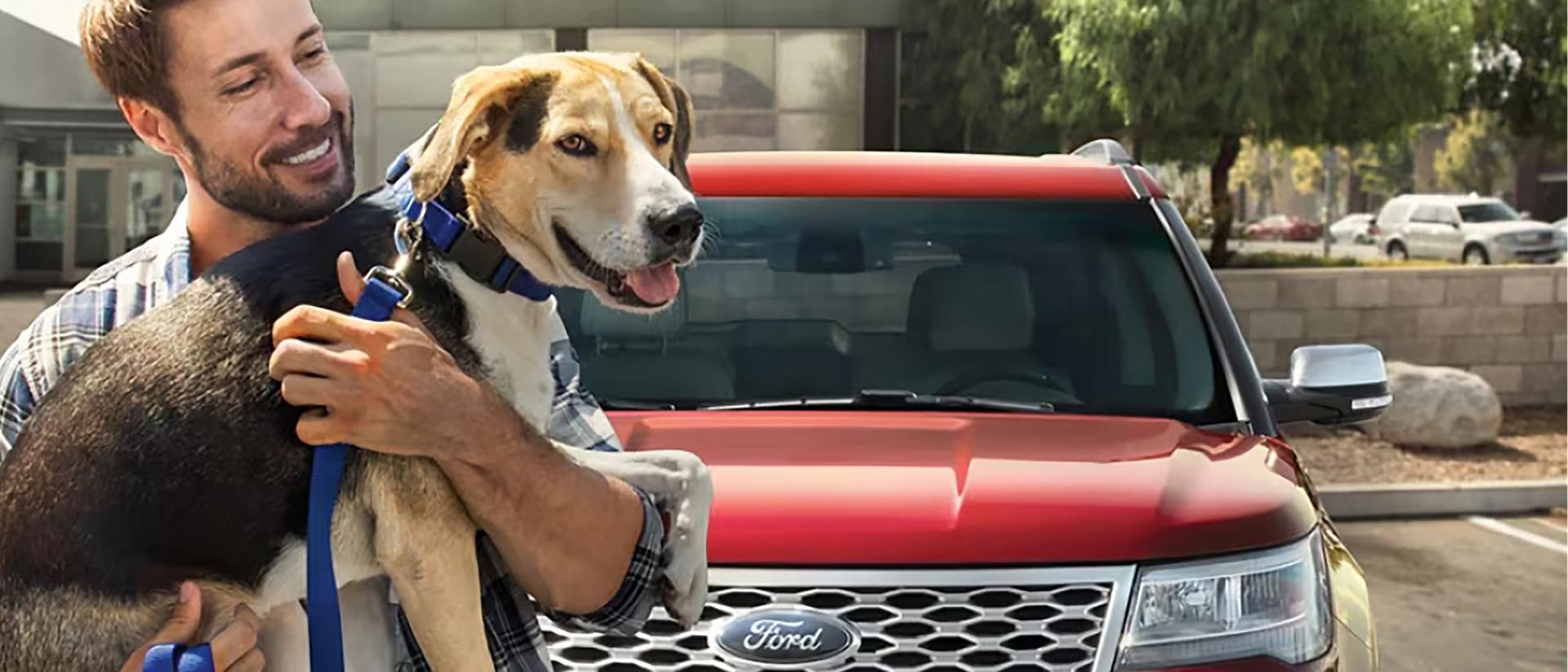 An owner holds their dog in front of their Ford vehicle