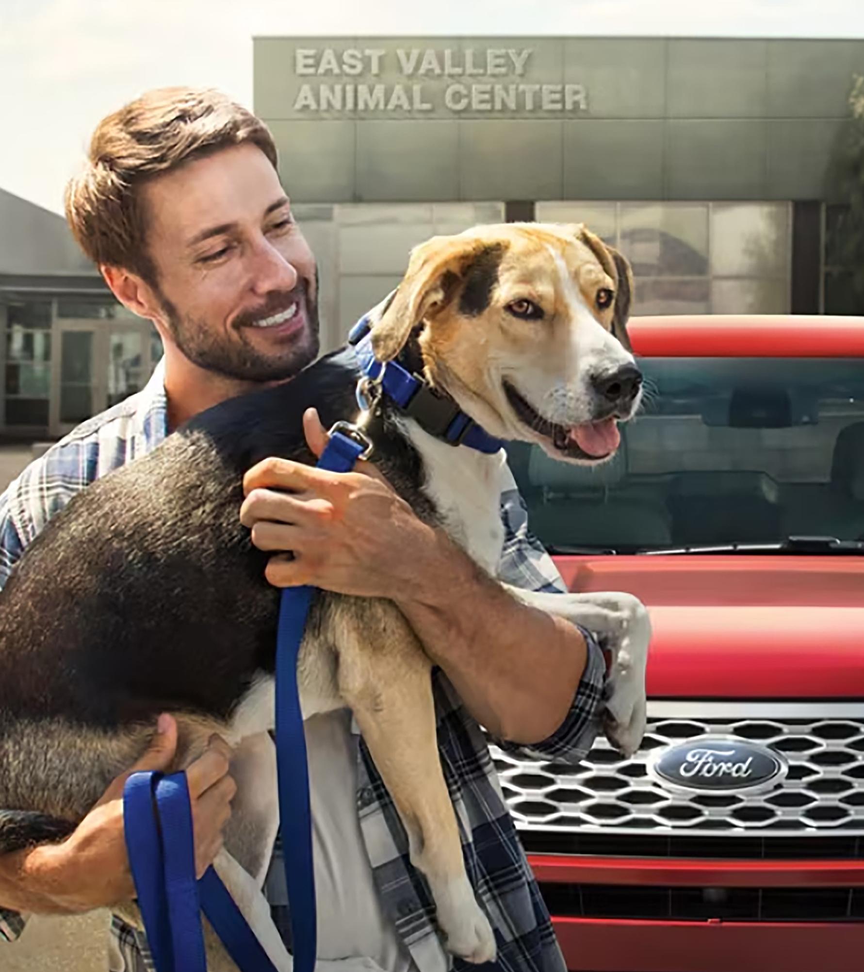 An owner holds their dog in front of their Ford vehicle