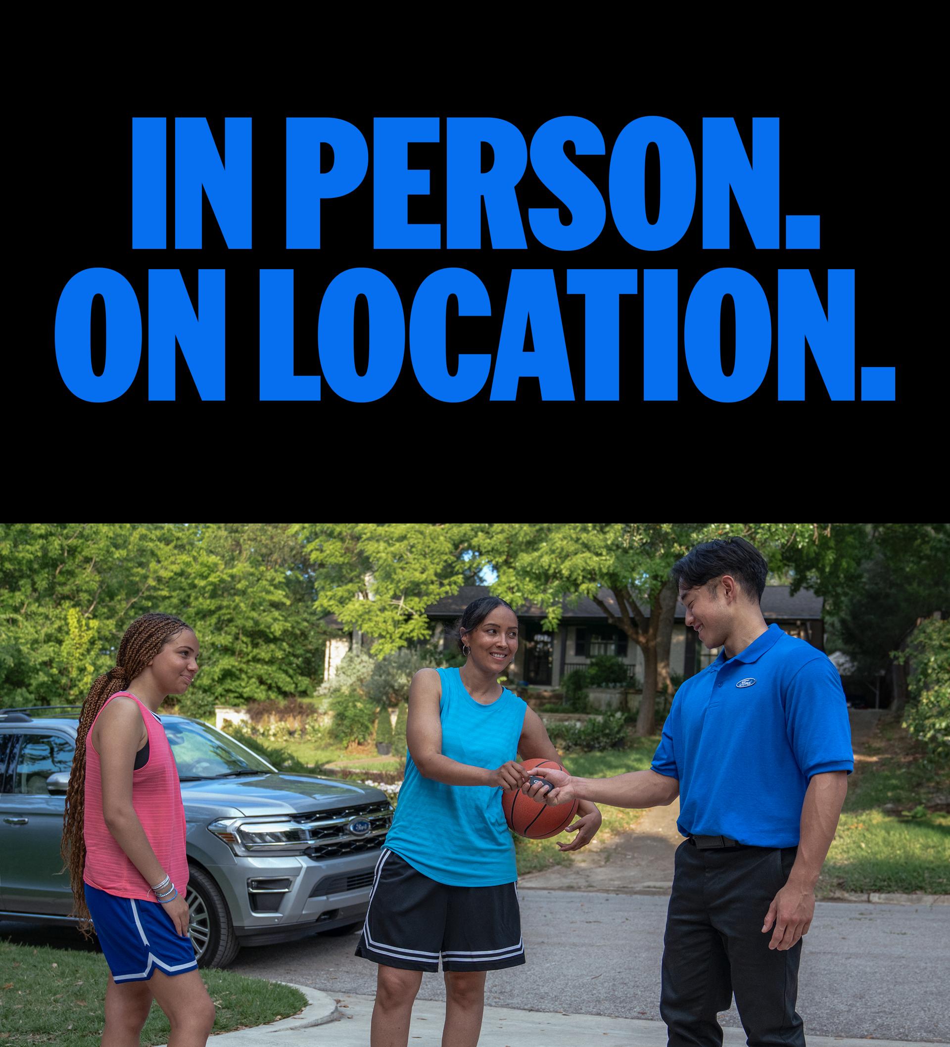 Two young people standing in the driveway talking to a Ford service tech