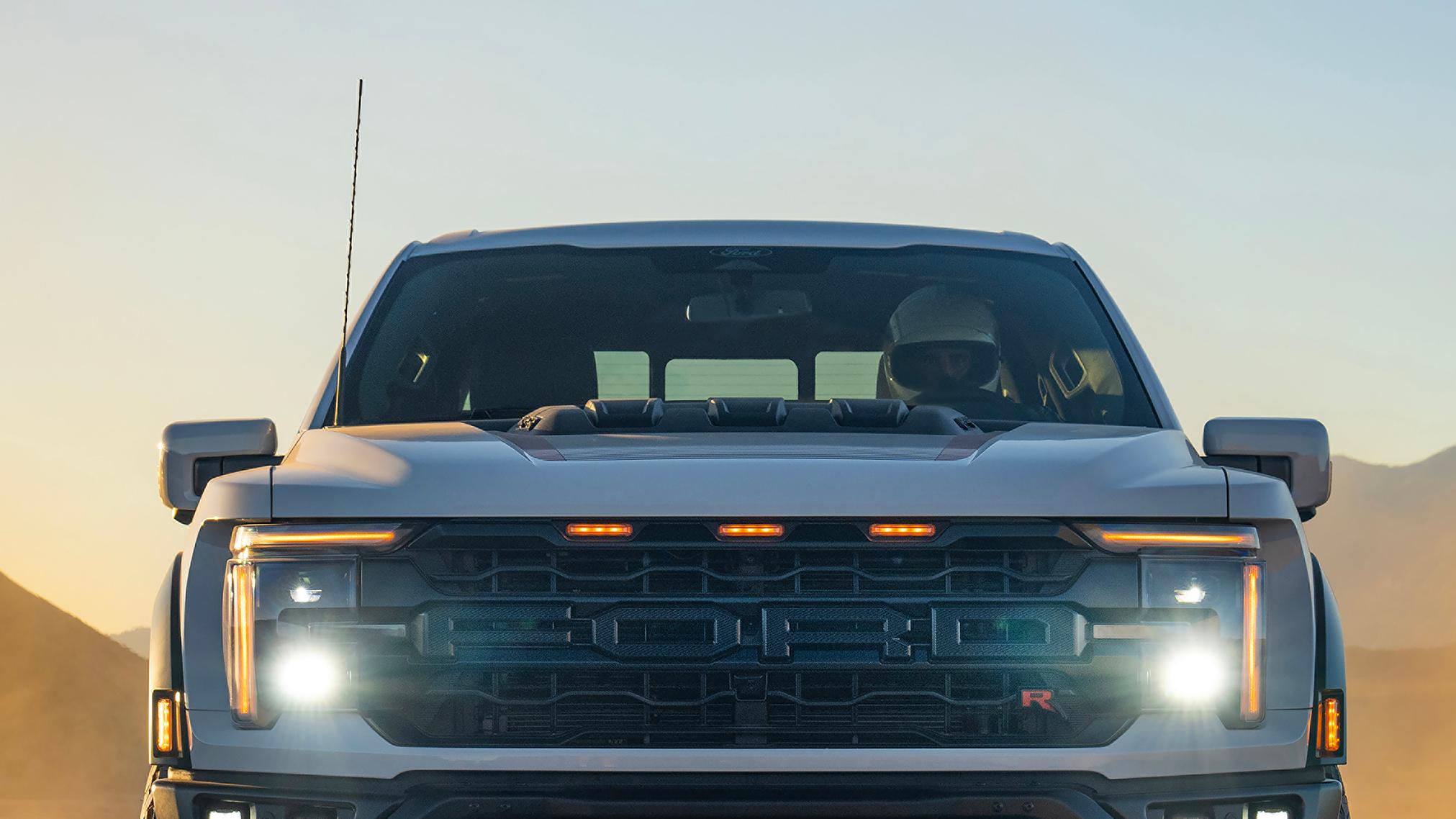 Close-up view of the grille and headlamp of a 2026 Ford F-150® Raptor® truck being driven in the desert