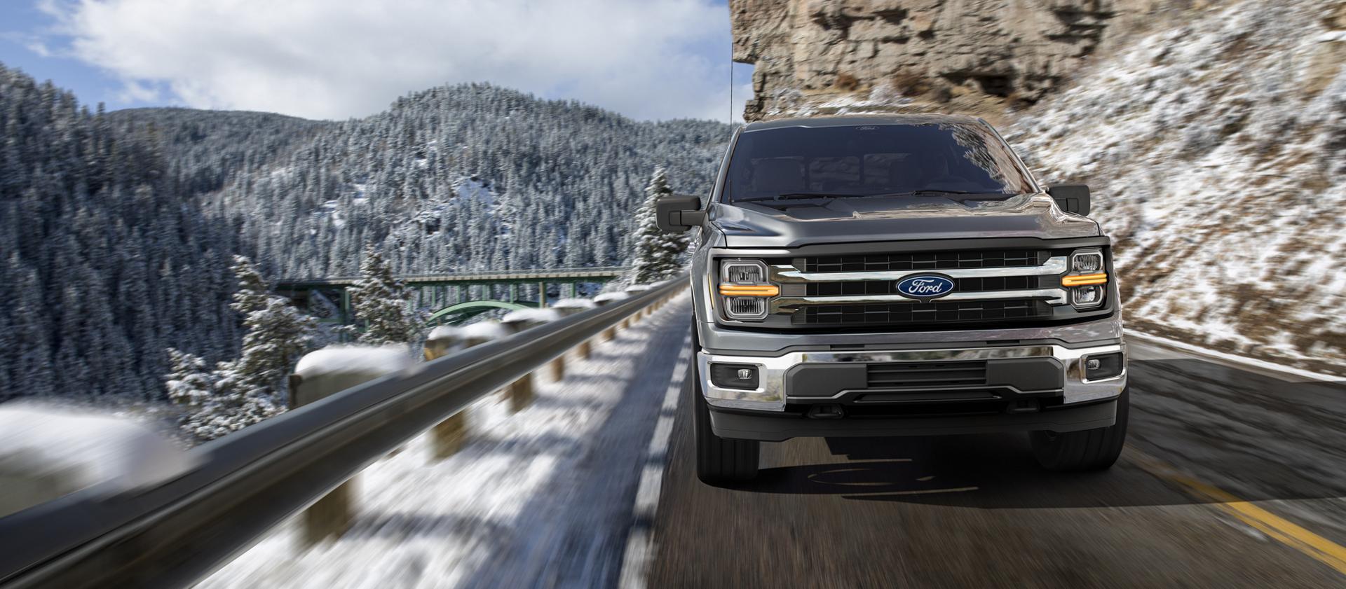 2027 Ford F-150® XLT model being driven on a mountain roadway with snow-covered mountains