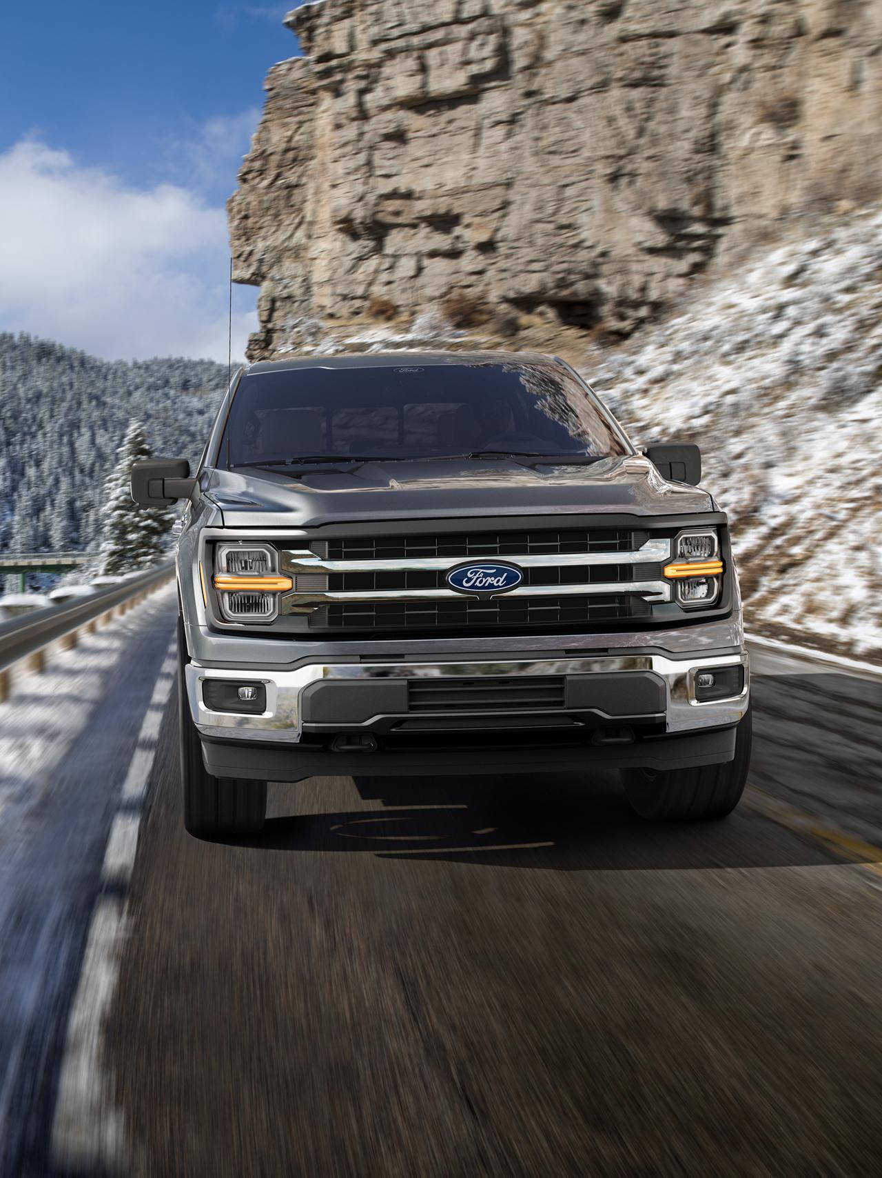 2027 Ford F-150® XLT model being driven on a mountain roadway with snow-covered mountains