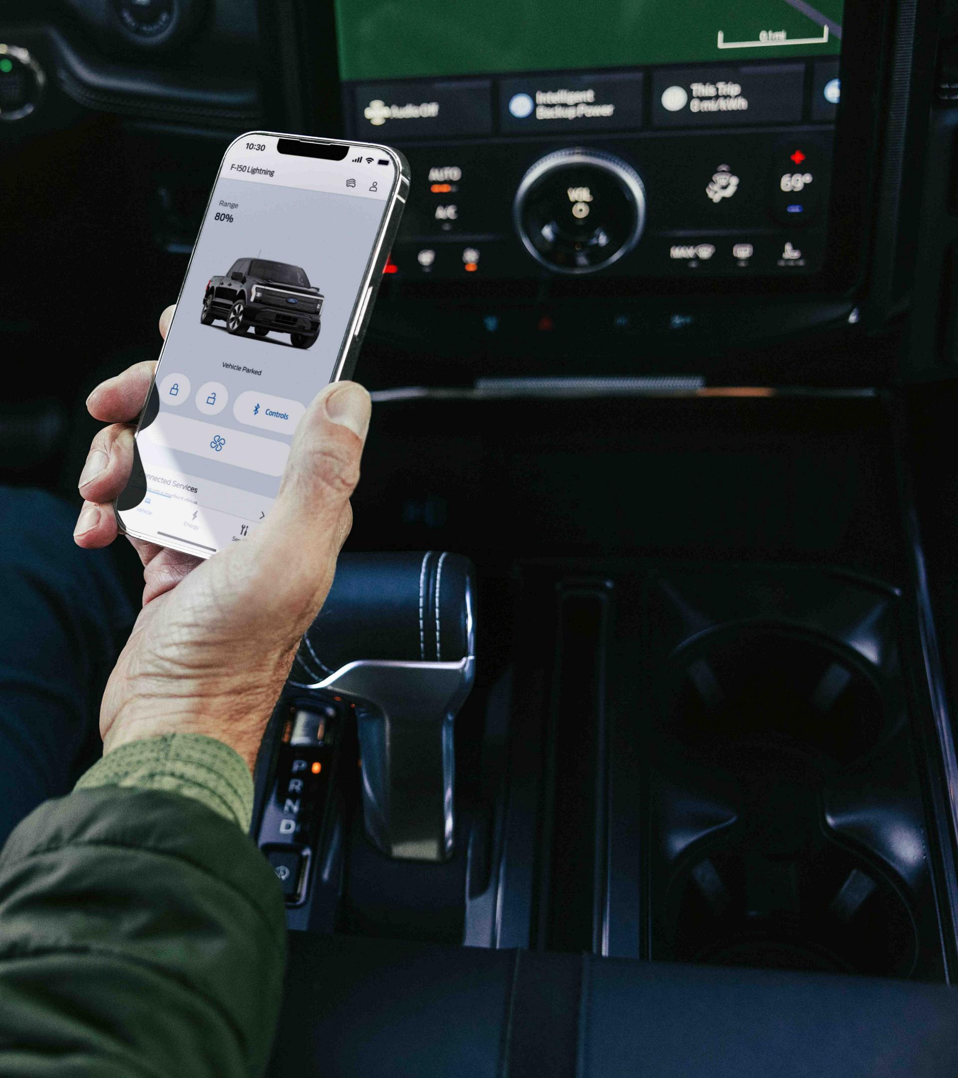 A Ford F-150 Lightning® truck driver looks at the FordPass® app on their phone while the truck is parked