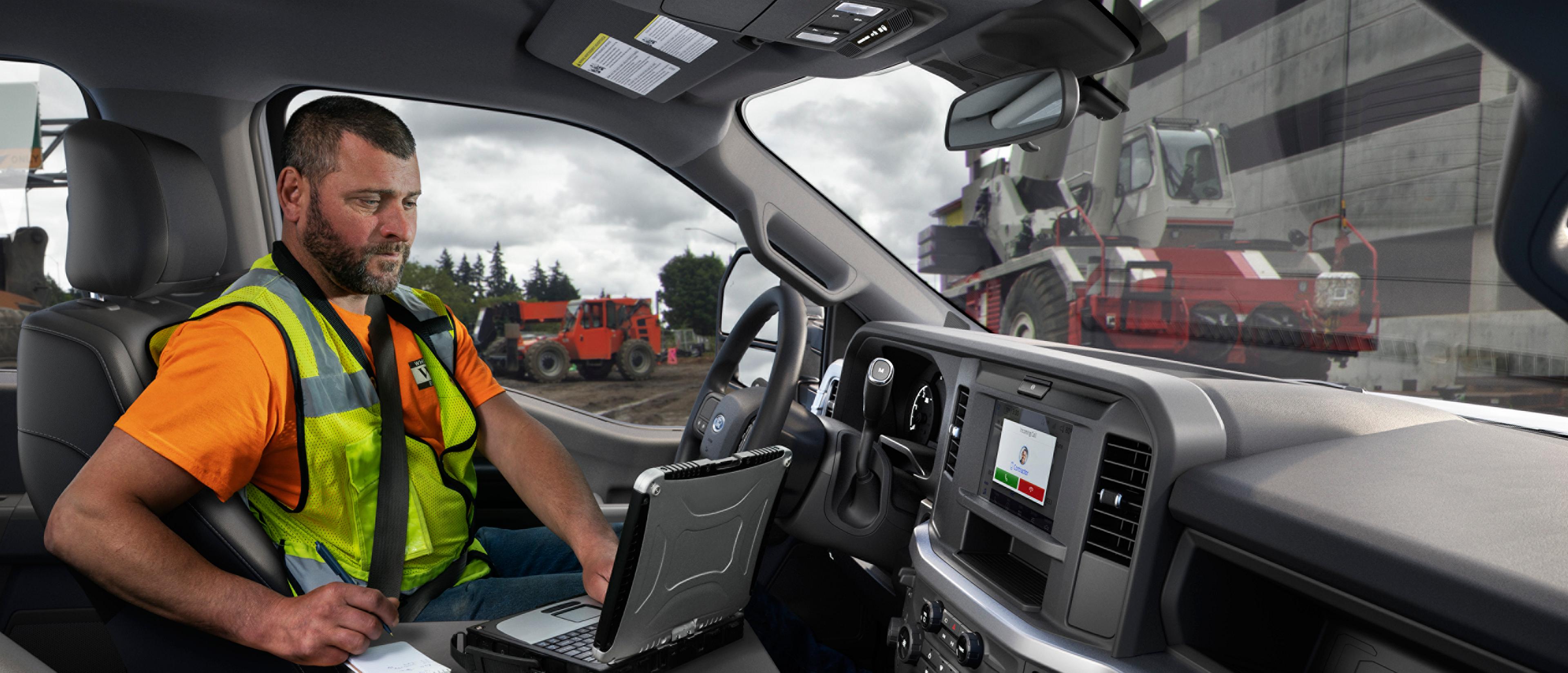 A person inside the cabin of their 2027 Ford Super Duty® truck using a laptop with the interior work surface