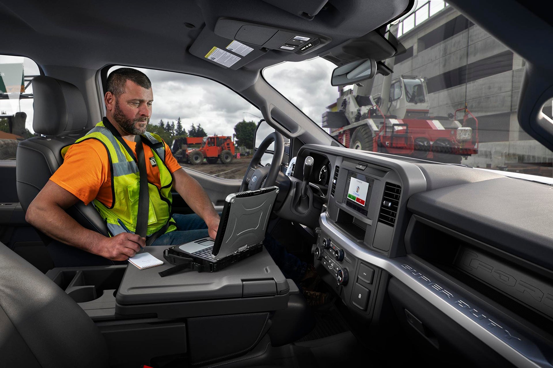 Worker using a laptop on the fold-out console inside a Ford Super Duty F-250 XL at a job site
