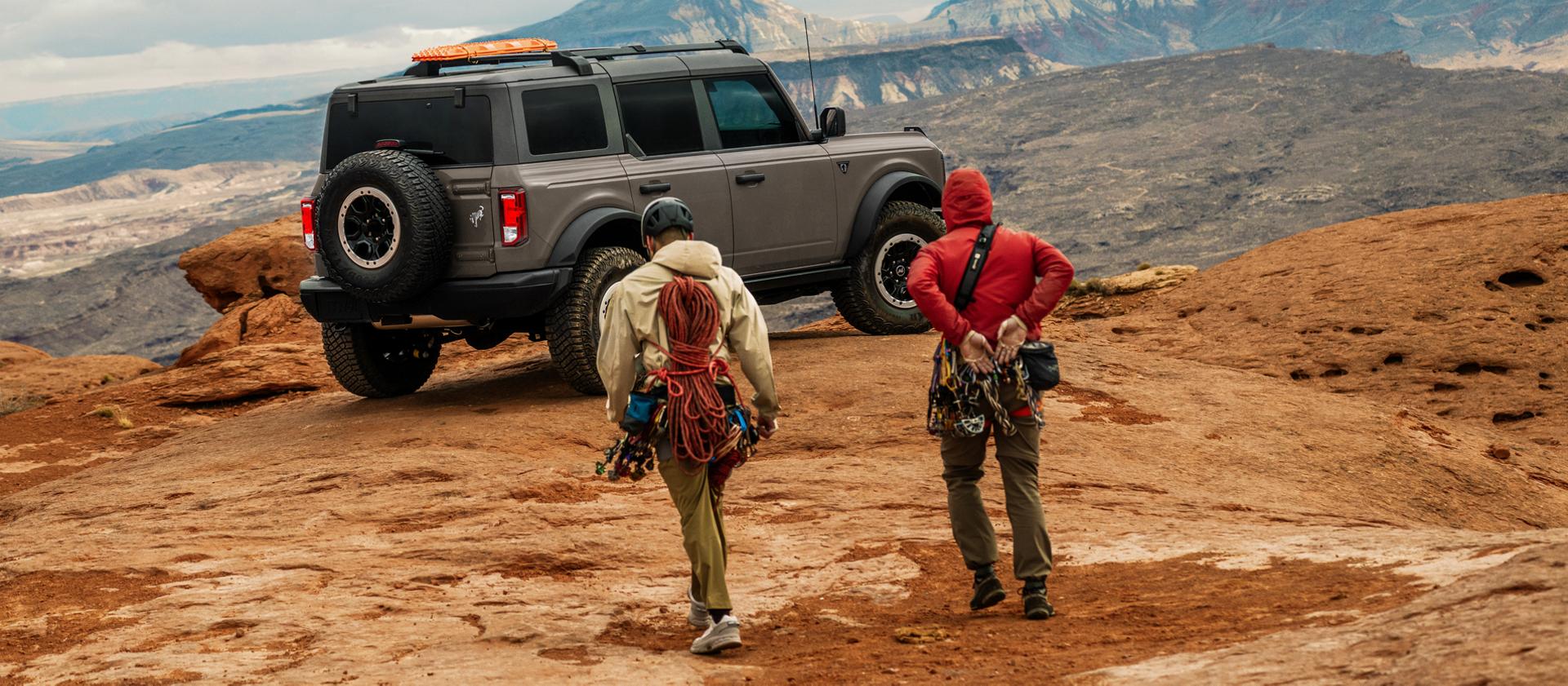 Two hikers approaching a 2026 Ford Bronco® SUV parked near a scenic overlook