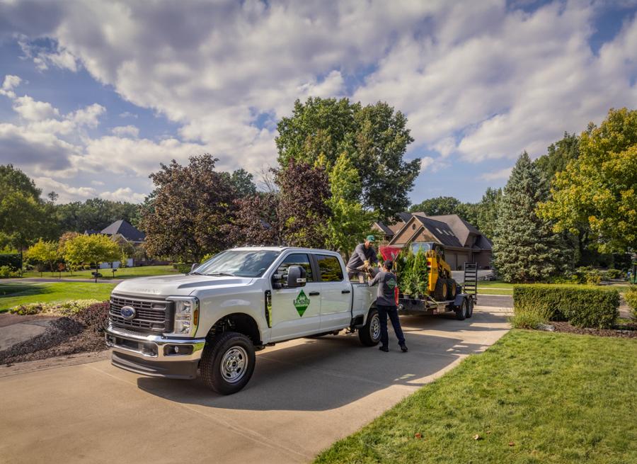 2026 Ford Super Duty® truck parked in a residential driveway towing a flatbed carrying landscape materials