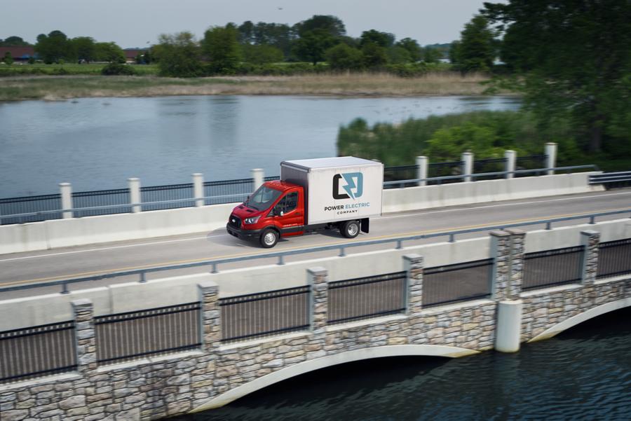 2025 Ford Transit® Chassis Cab model with box truck upfit being driven over a bridge with a lake in the background