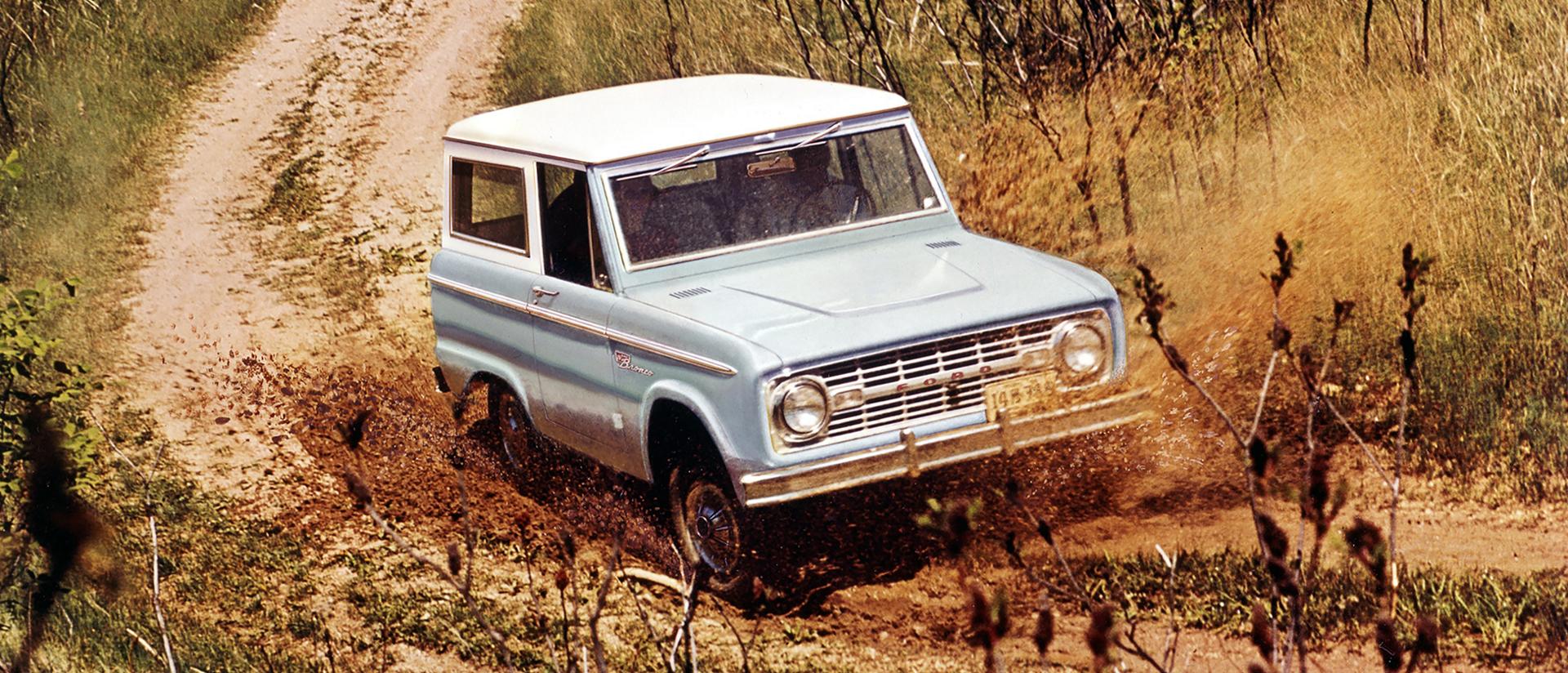A 1967 Ford Bronco® model being driven down a dusty dirt road