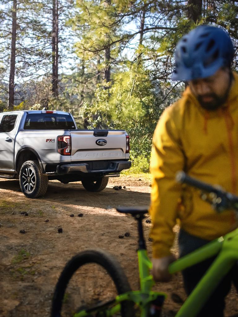 2026 Ford Ranger® Lariat® model parked in the woods. The truck's owner is pulling away on a bike