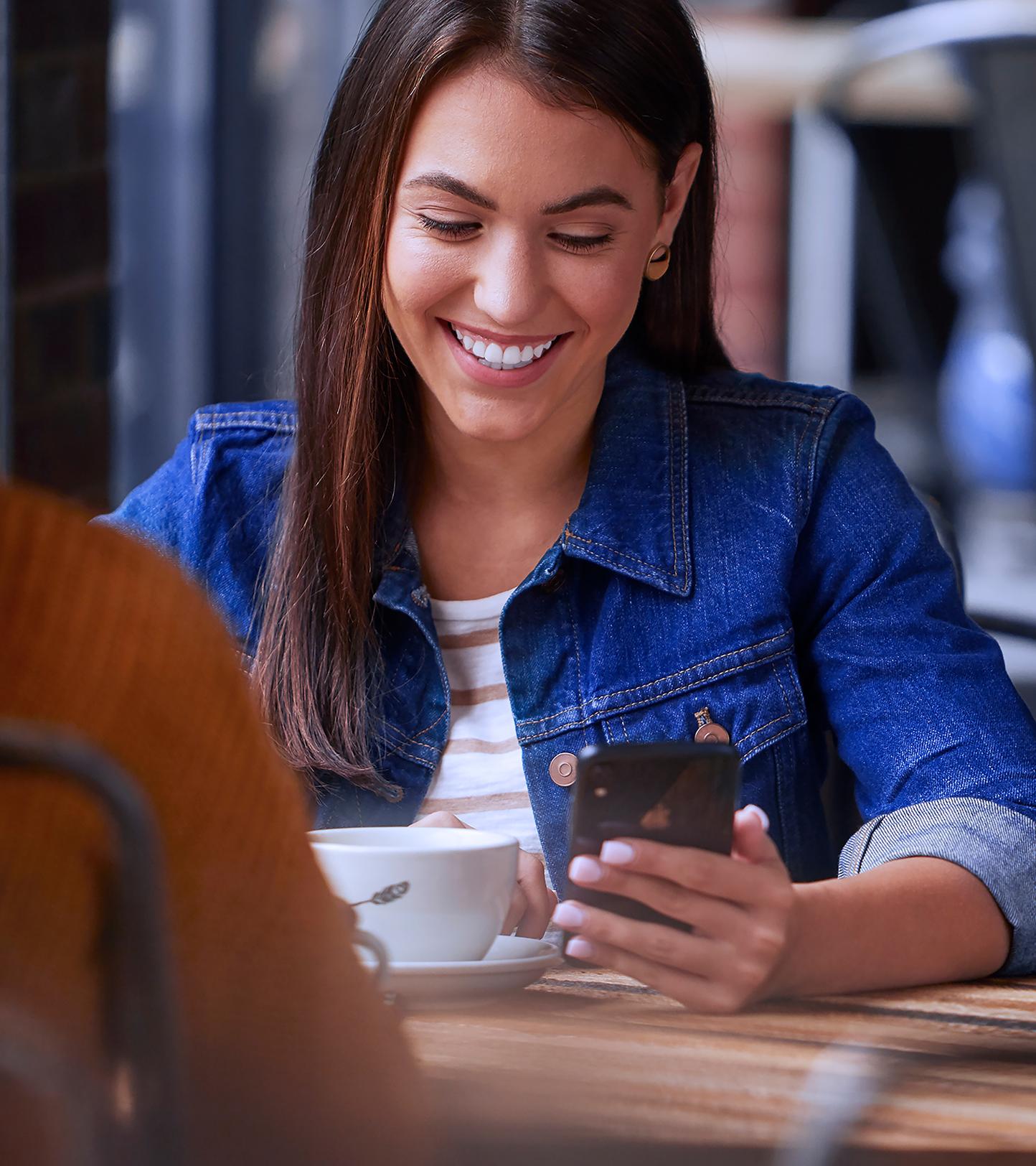 A person is sitting at a table holding a smartphone and smiling
