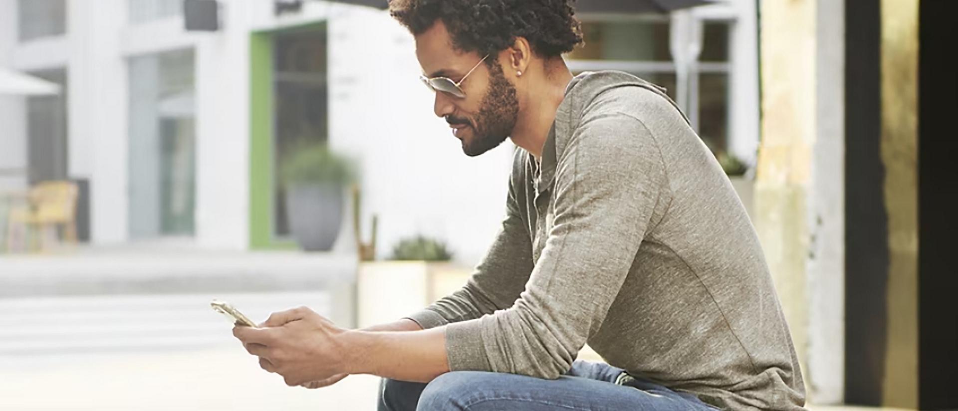 A person sits outside a modern building looking at their phone