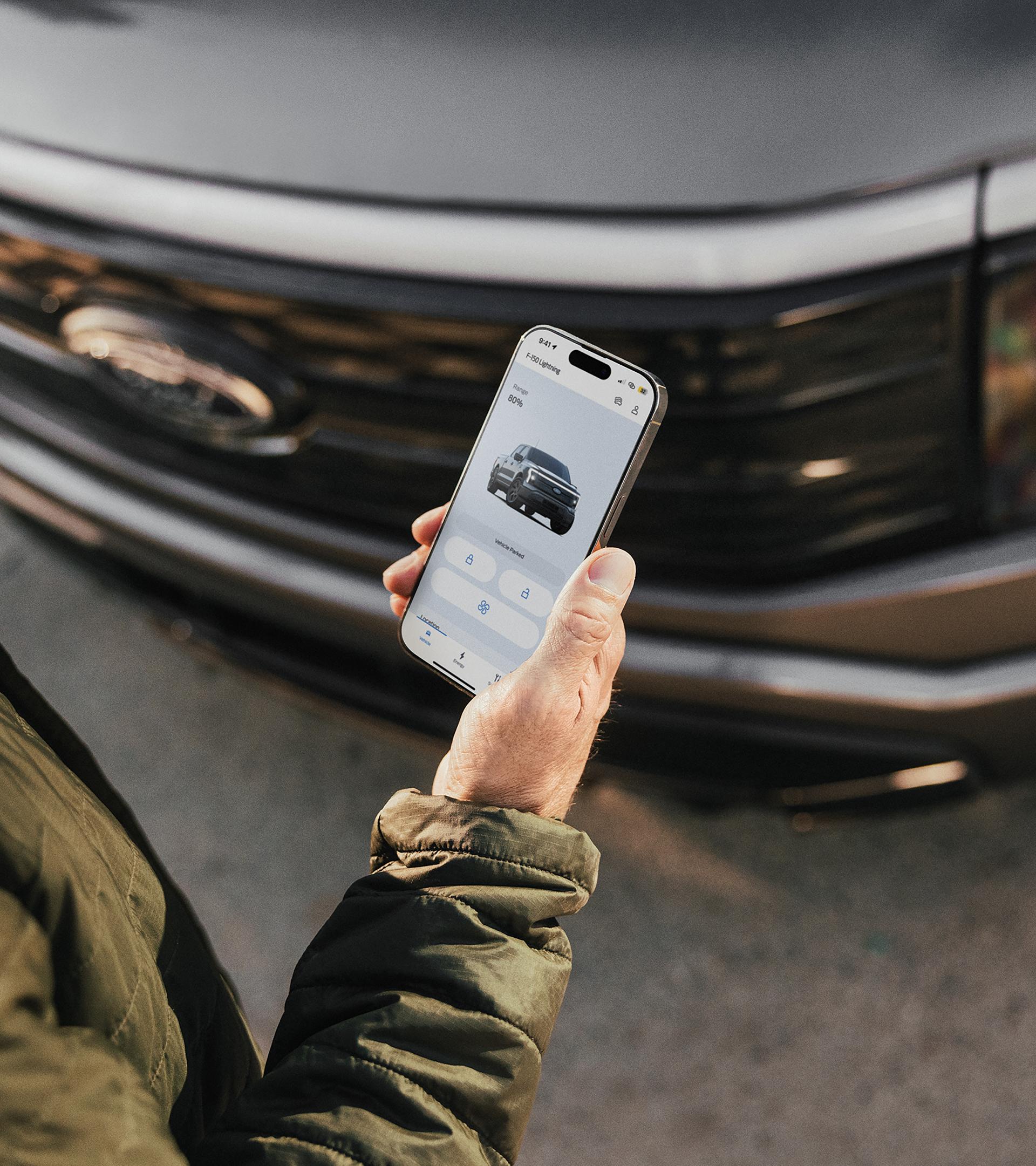 An owner stands in front of their 2024 Ford F-150 Lightning® truck and checks the charge level on their phone