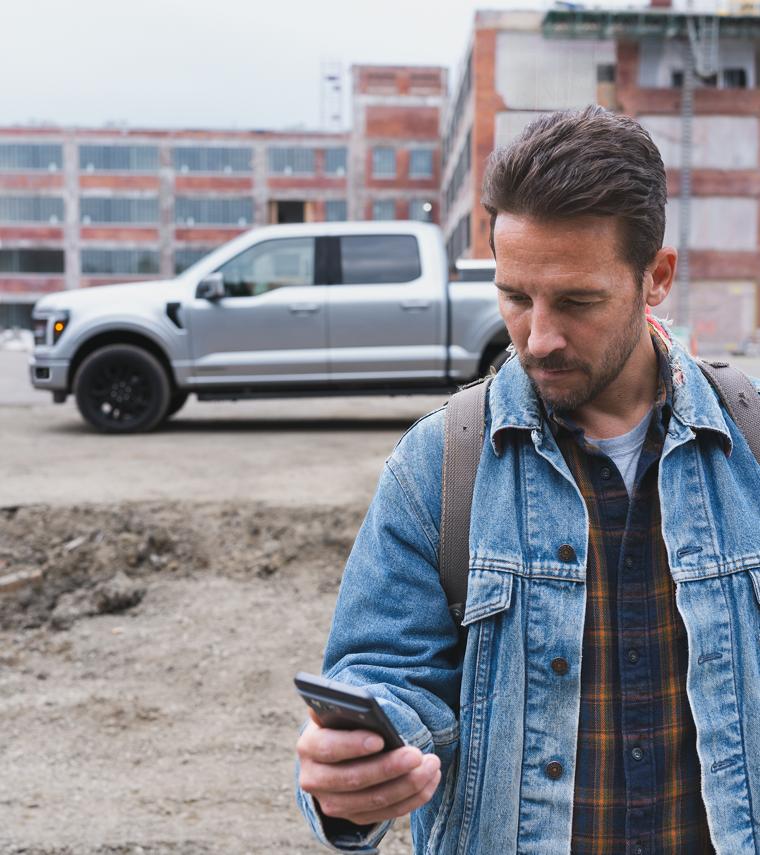 An exterior shot of a man looking at his phone while walking away from a gray 2026 Ford F-150® truck