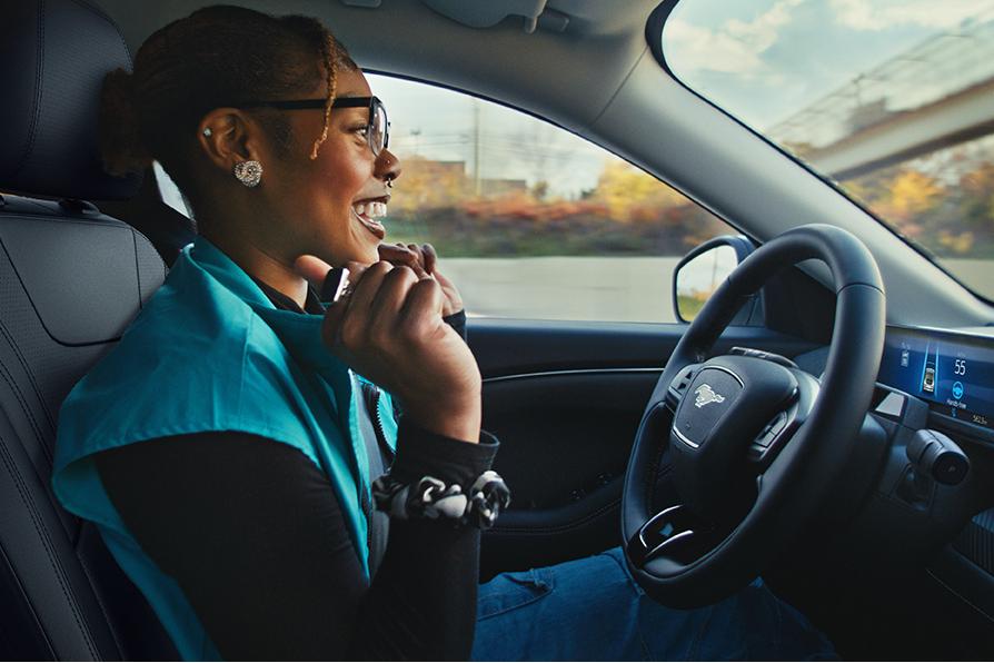A 2026 Ford Mustang Mach-E® driver raises their hands and smiles while driving hands-free on a divided highway