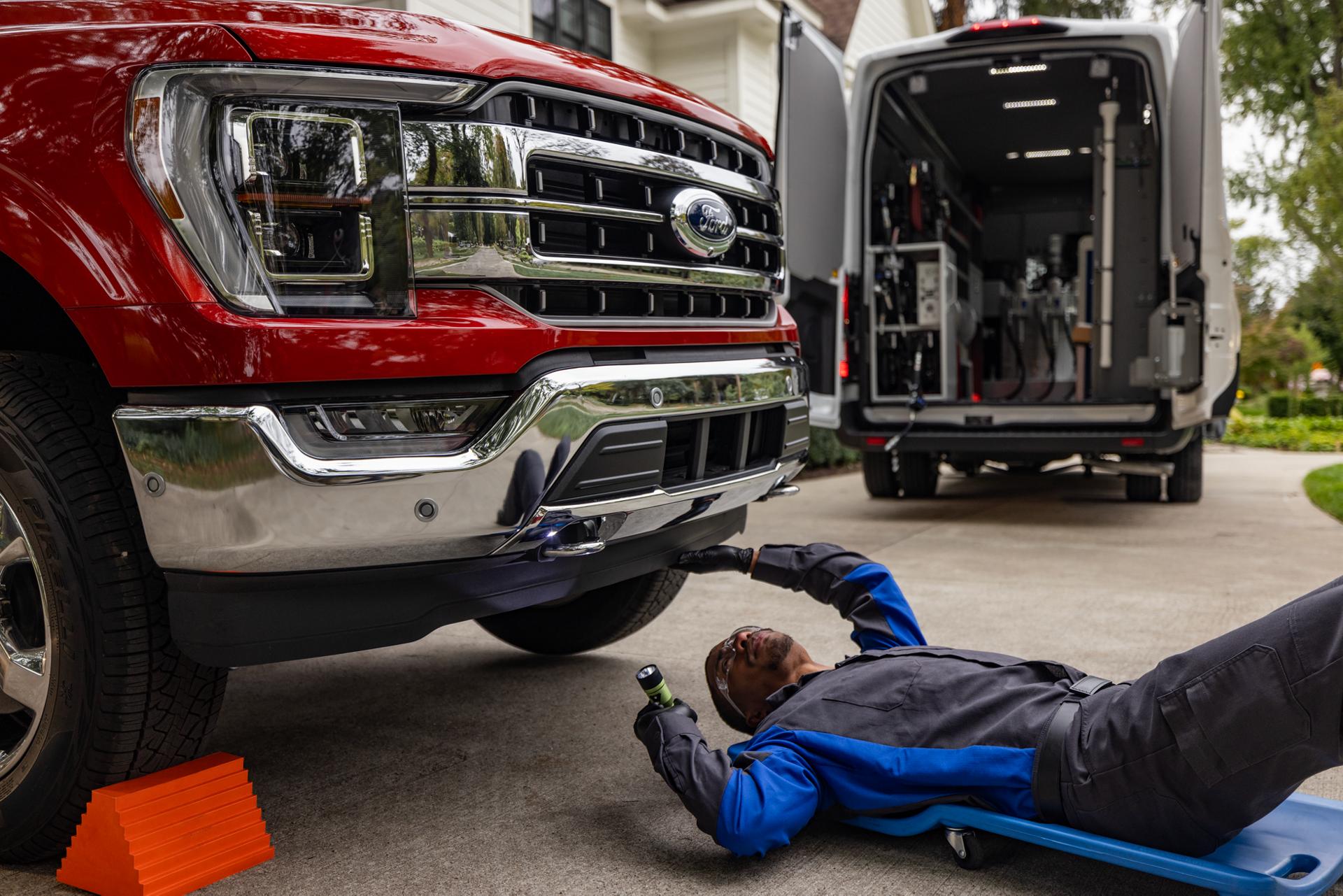 A Ford service technician is working in a driveway and rolls under the front of a Ford F-150® truck