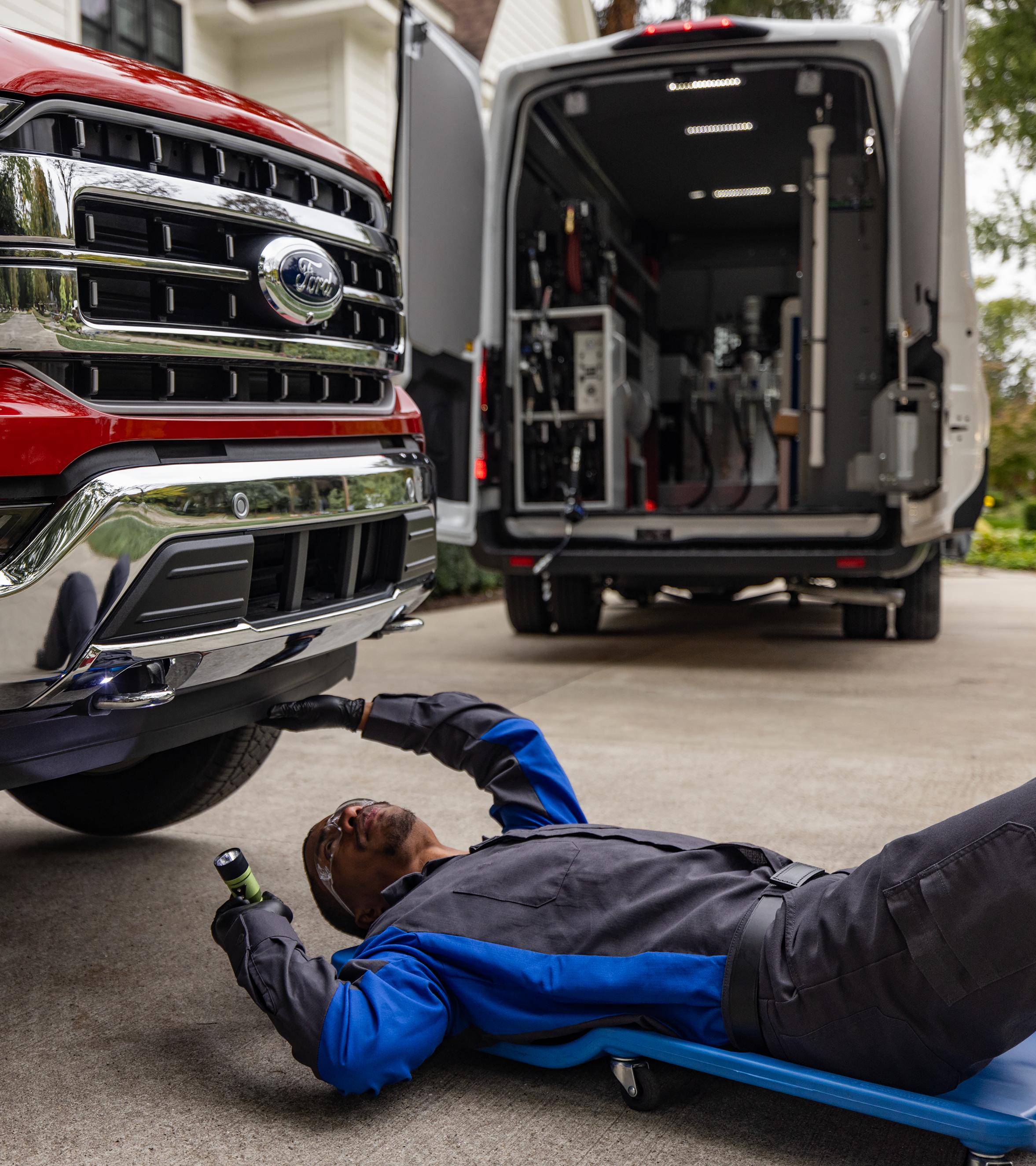 A Ford service technician is working in a driveway and rolls under the front of a Ford F-150® truck