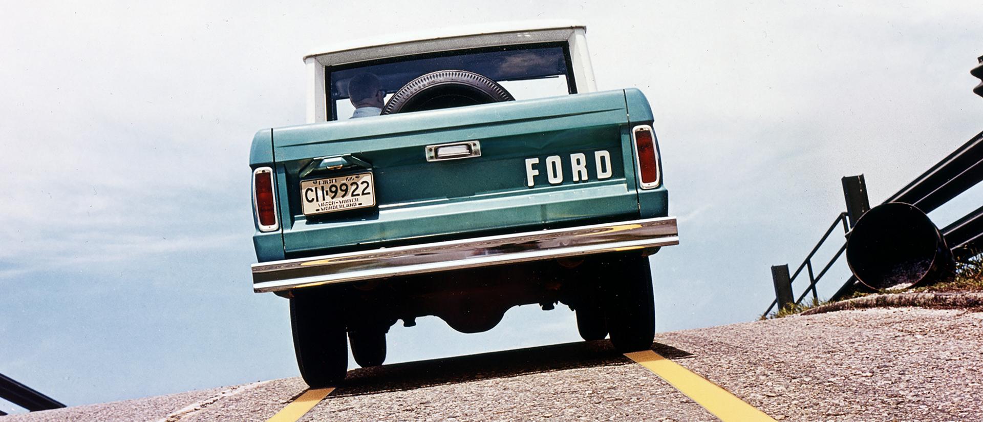 A 1967 Ford Bronco® being driven on a road pictured from behind the vehicle