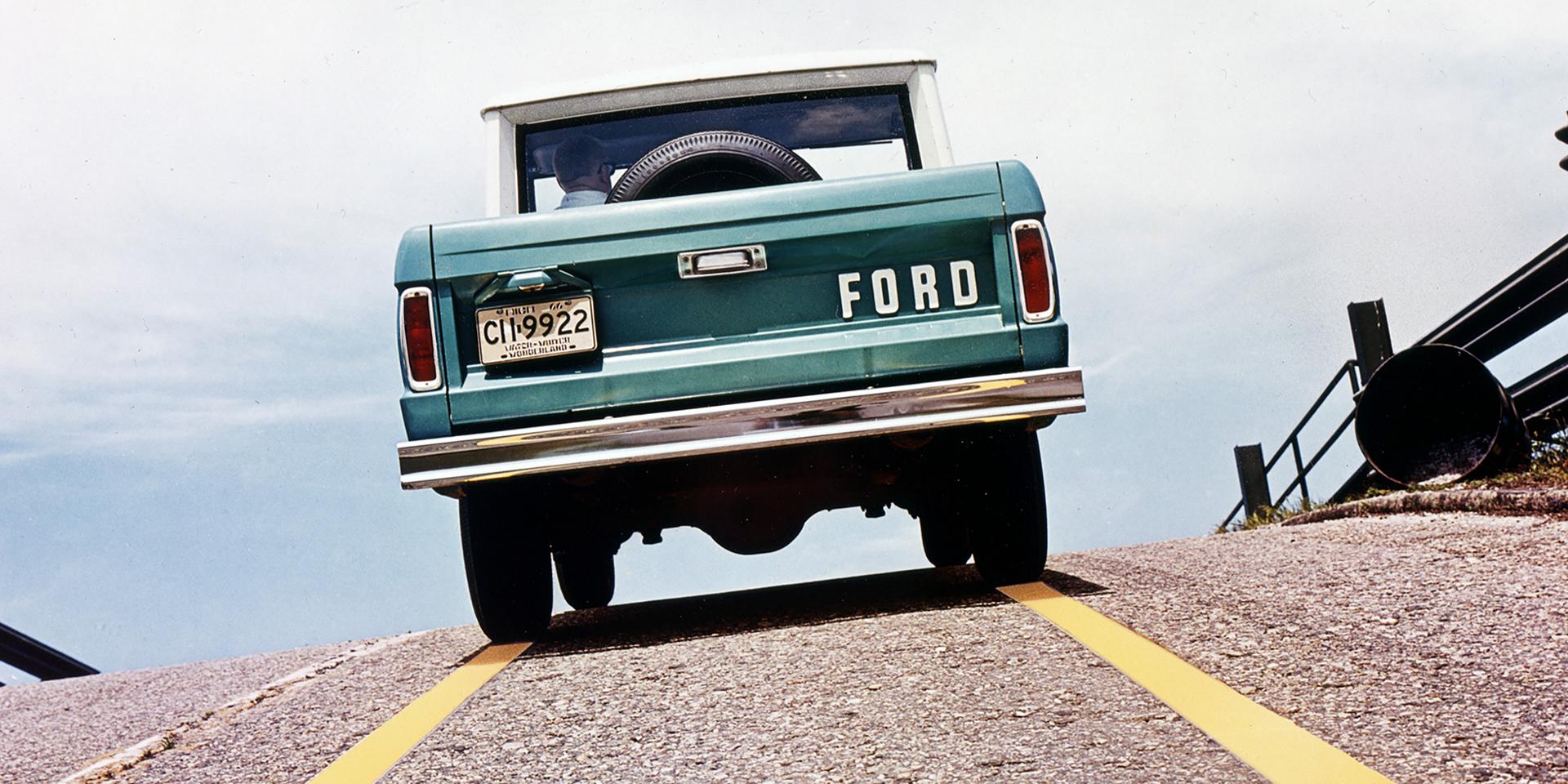 A 1967 Ford Bronco® being driven on a road pictured from behind the vehicle