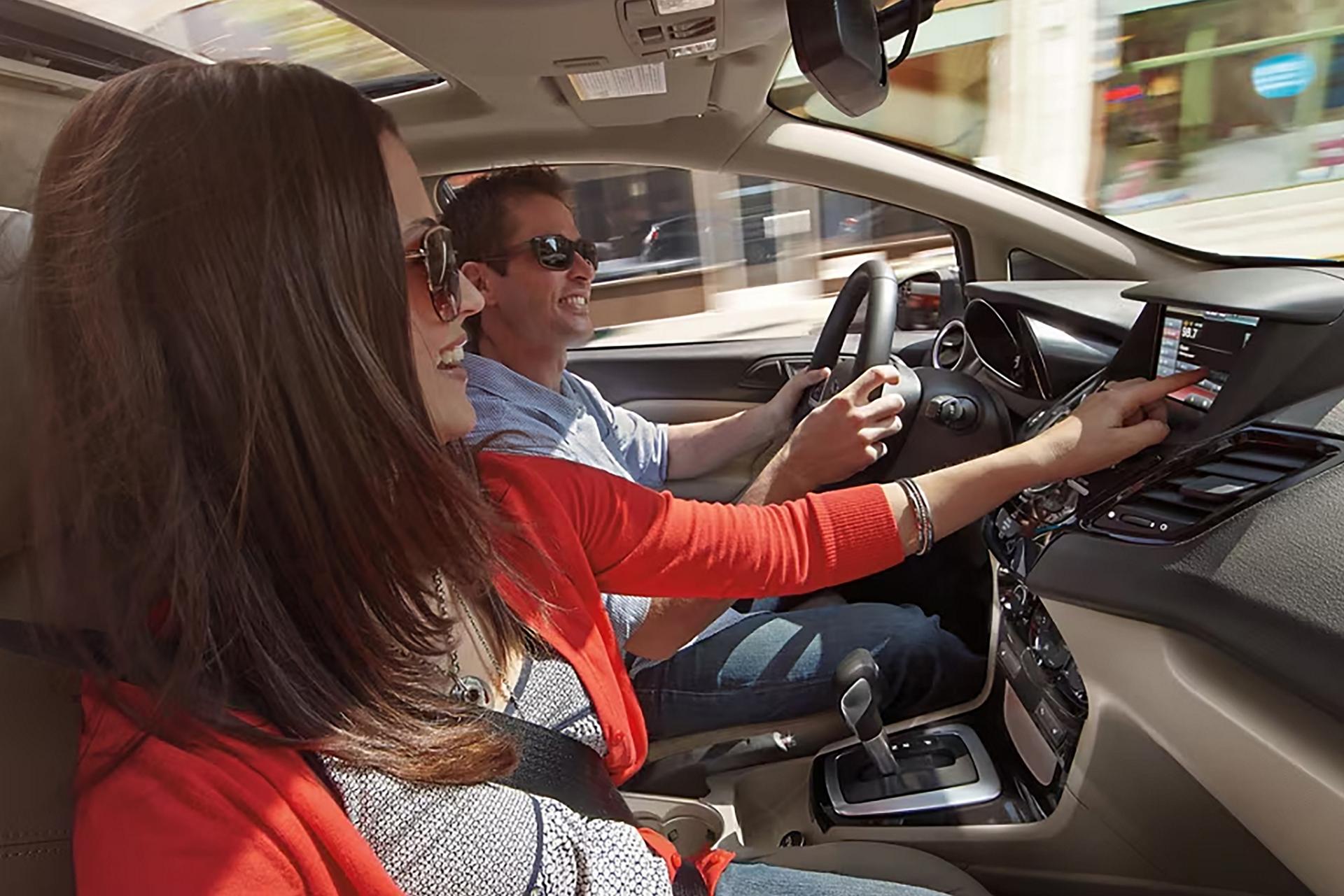 A passenger smiles while adjusting the radio and cruising downtown in a Ford vehicle