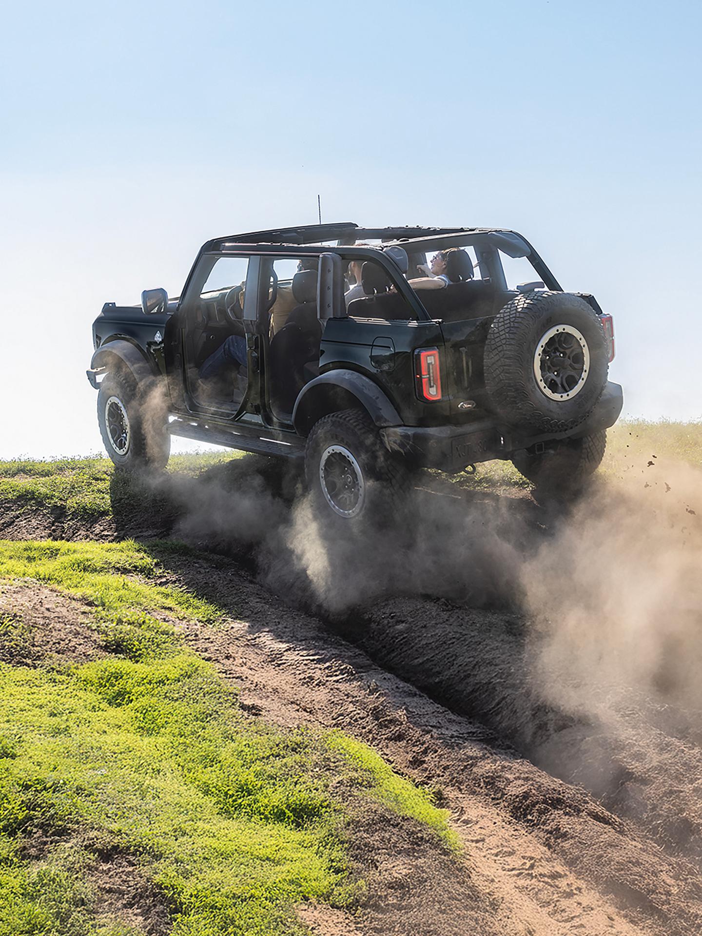 A 2026 Ford Bronco® SUV being driven on a muddy hillside with doors and roof removed