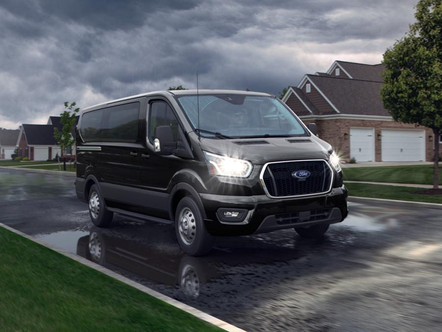 A Ford Transit cargo van driving on a suburban road.