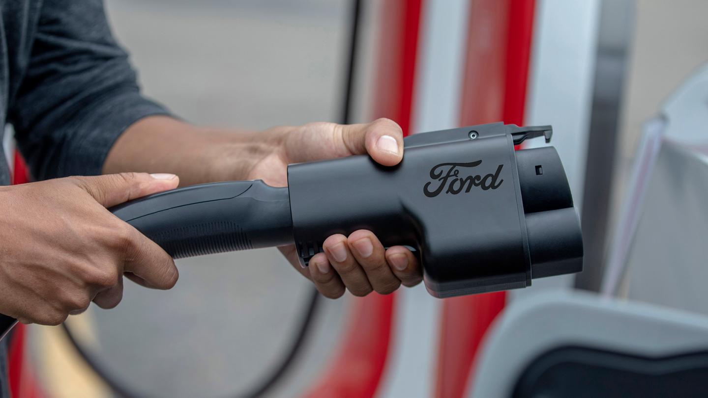 Person using th NACS charging adapter for a Tesla Supercharger