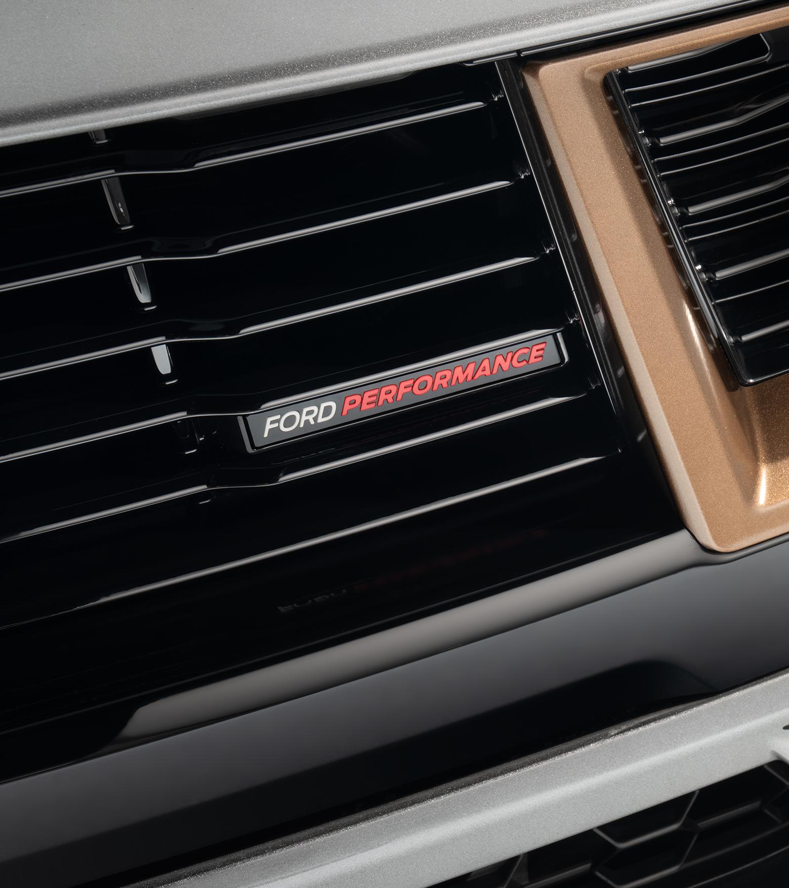Close-up of the Ford Performance badge in white and red lettering set into the gloss black grille bars beside the bronze insert