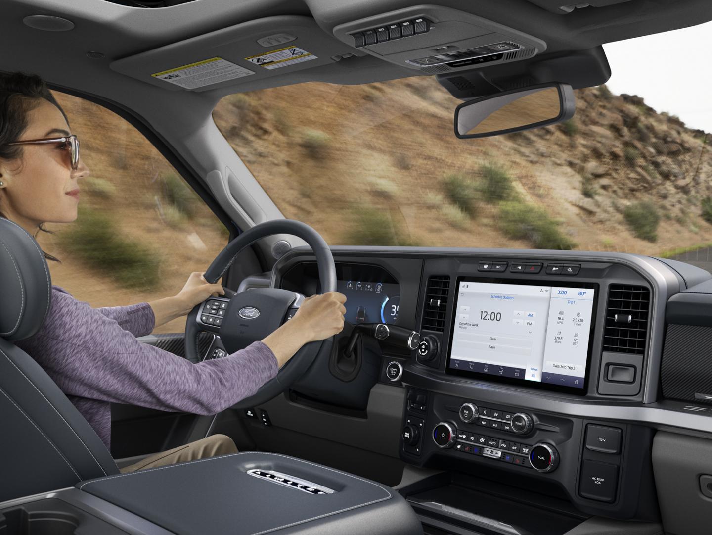 A woman driving a Ford Super Duty pickup truck. The SYNC touchscreen is displaying a menu.