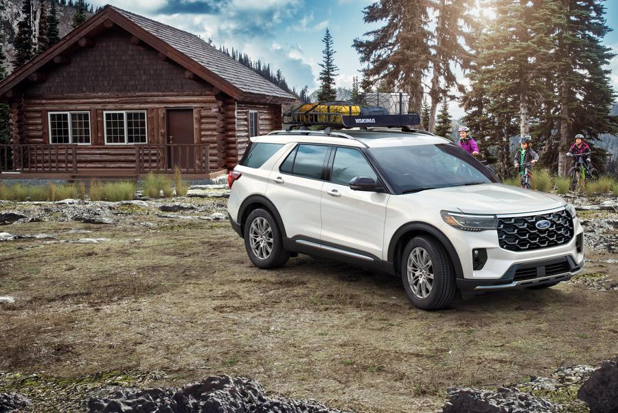 White 2025 Ford Explorer® parked outside a rustic cabin as a family on bikes approaches