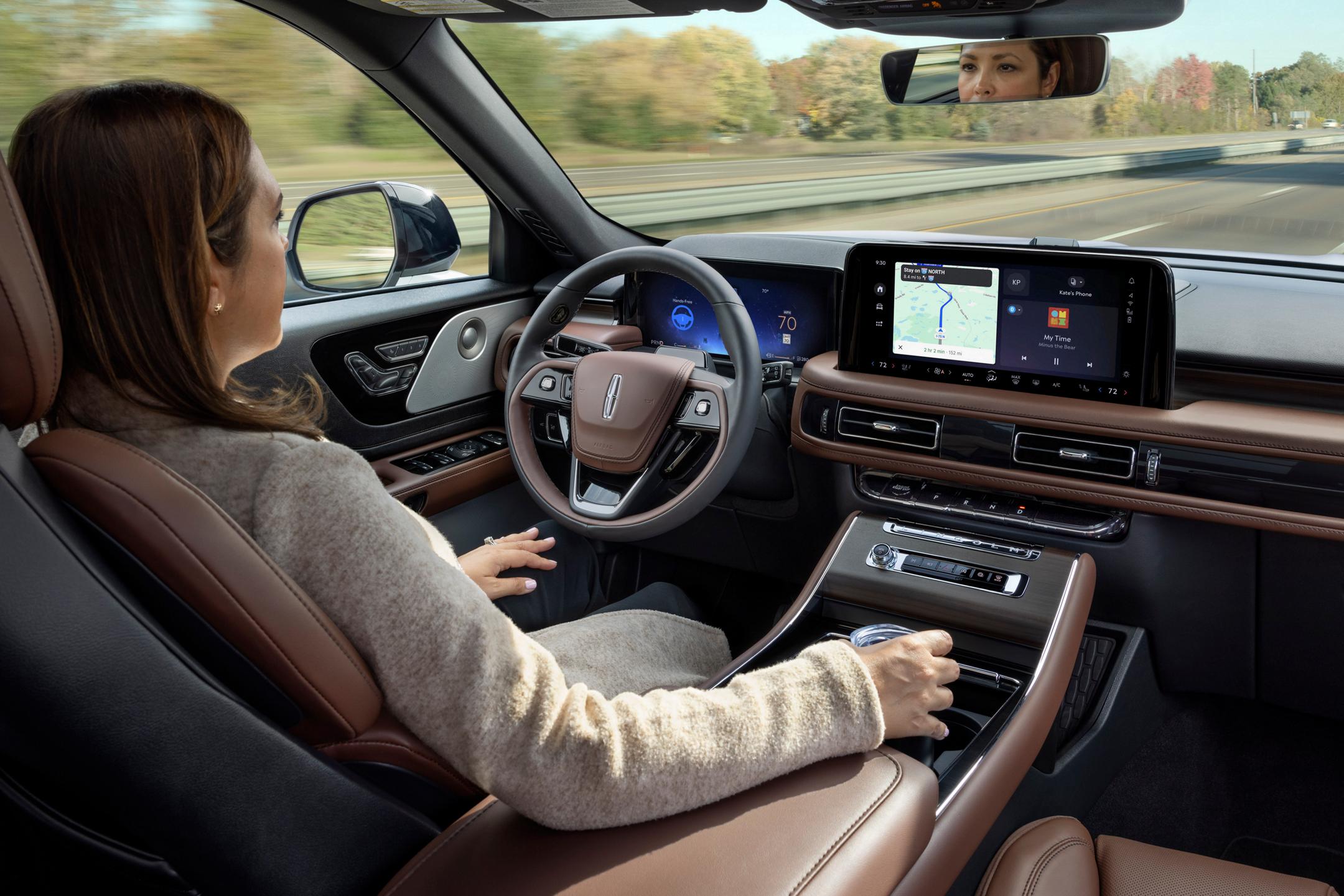 A 2025 Lincoln Aviator is being driven hands-free on a highway near a forest