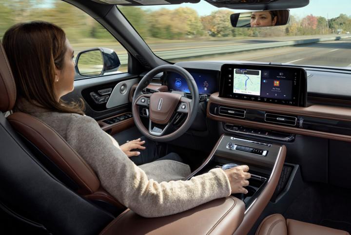 Un Lincoln Aviator 2025 conduit en mode mains libres sur une autoroute près d’une forêt
