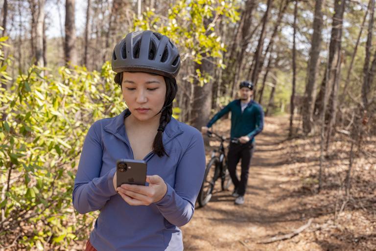 Woman checking her phone while she and a man walk their bikes on a trail