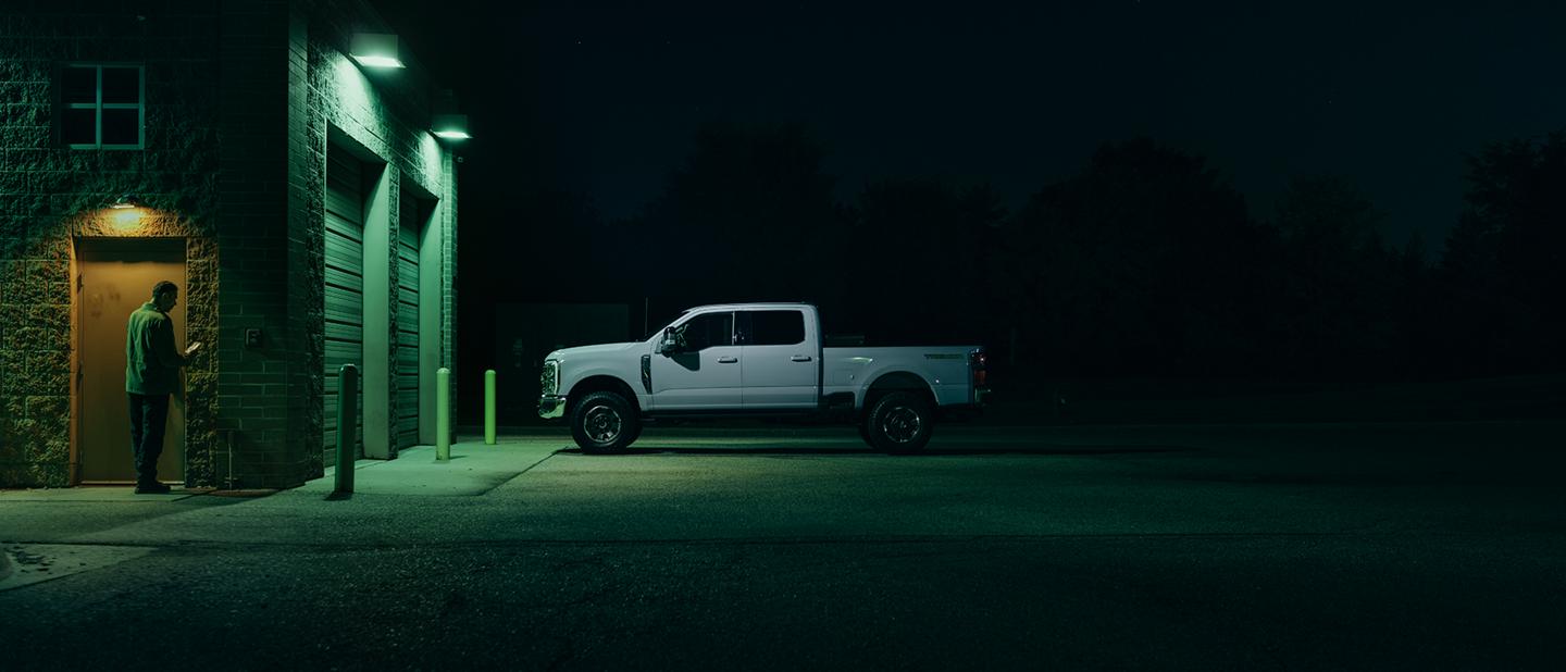 Man using phone in parking lot at night, near truck