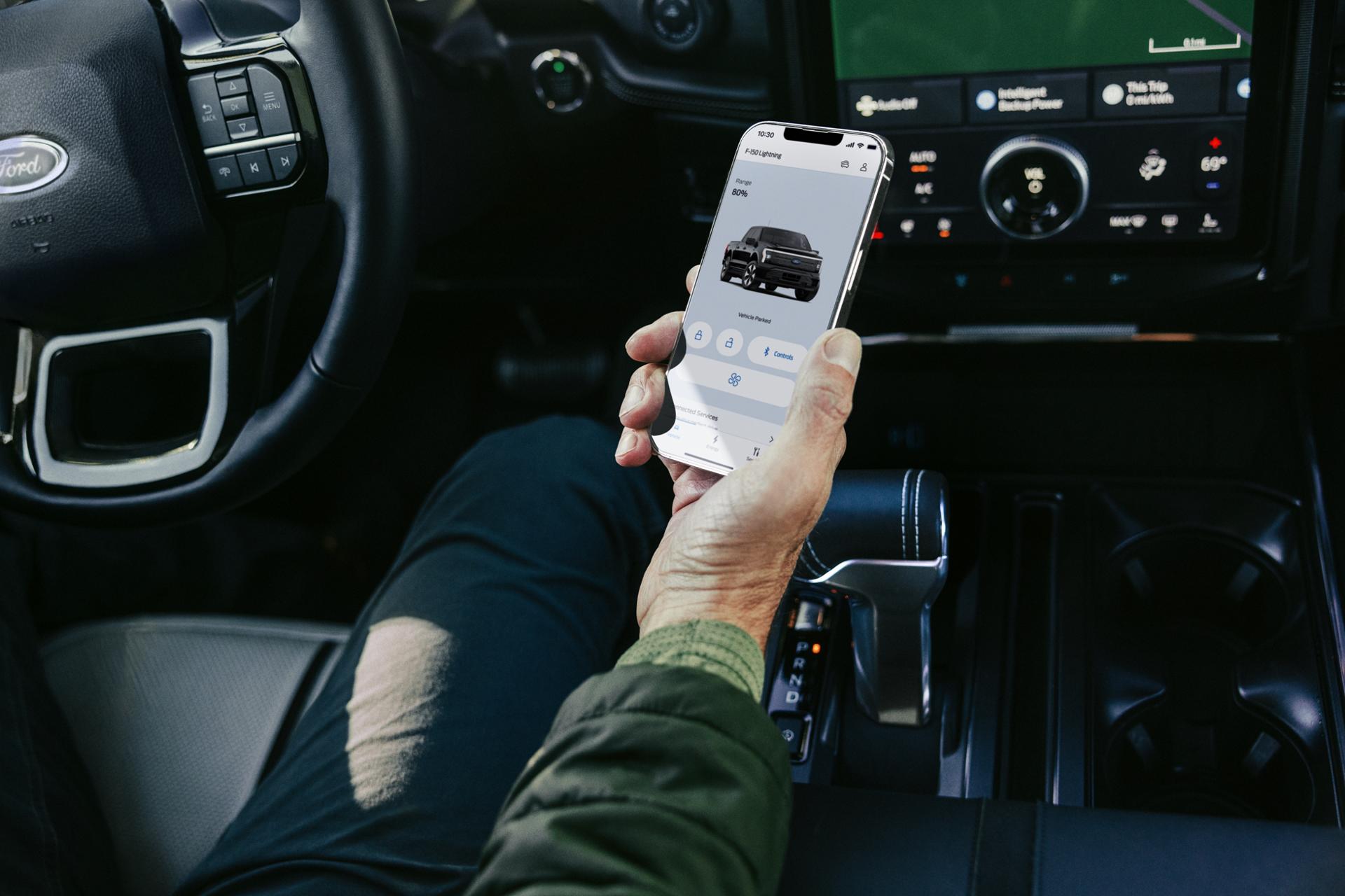 Person holding a phone displaying the FordPass® app inside a Ford electric vehicle
