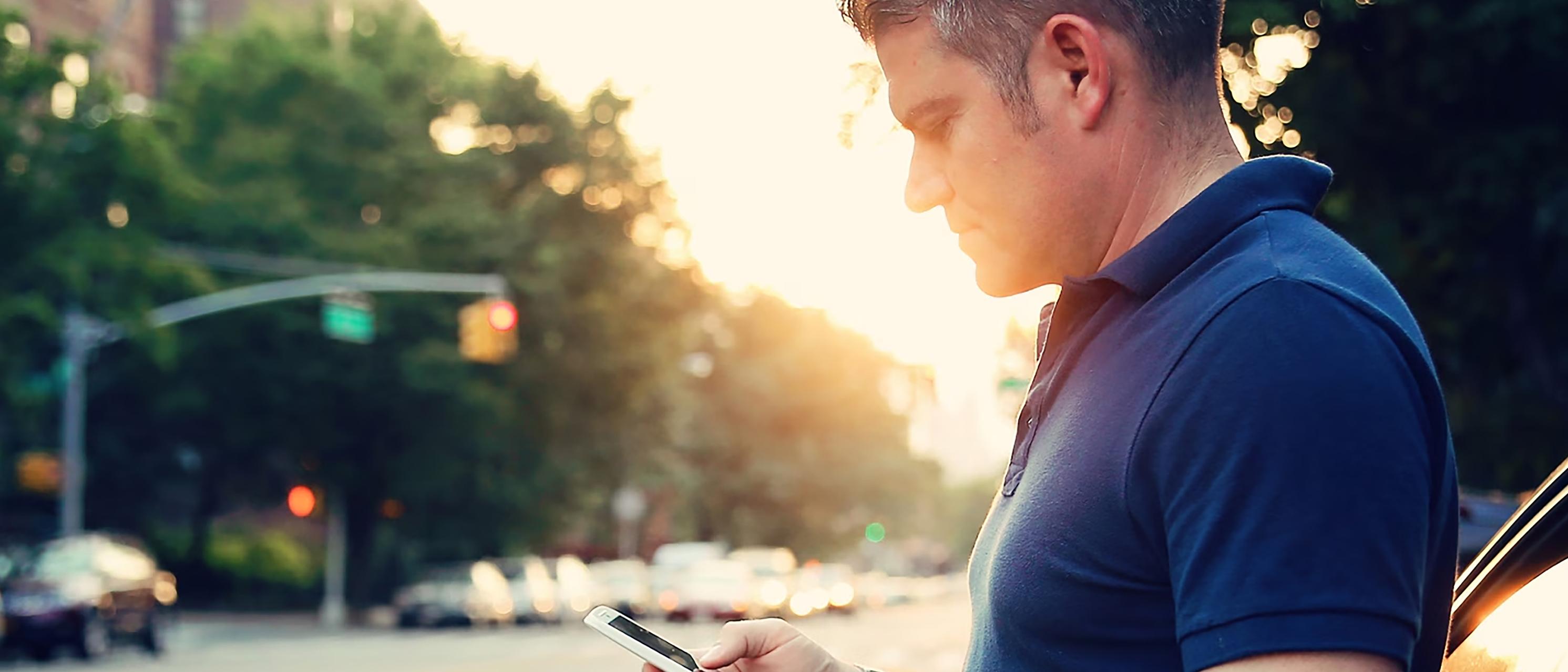 A person stands outside a vehicle parked roadside and glances at their phone
