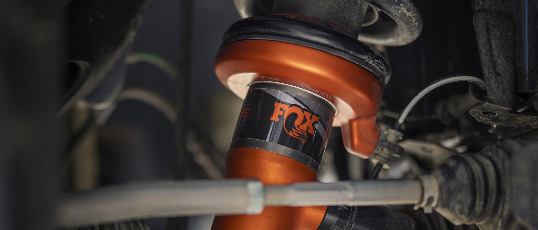 A close-up product shot of a high-performance orange FOX™ Live Valve shock absorber
