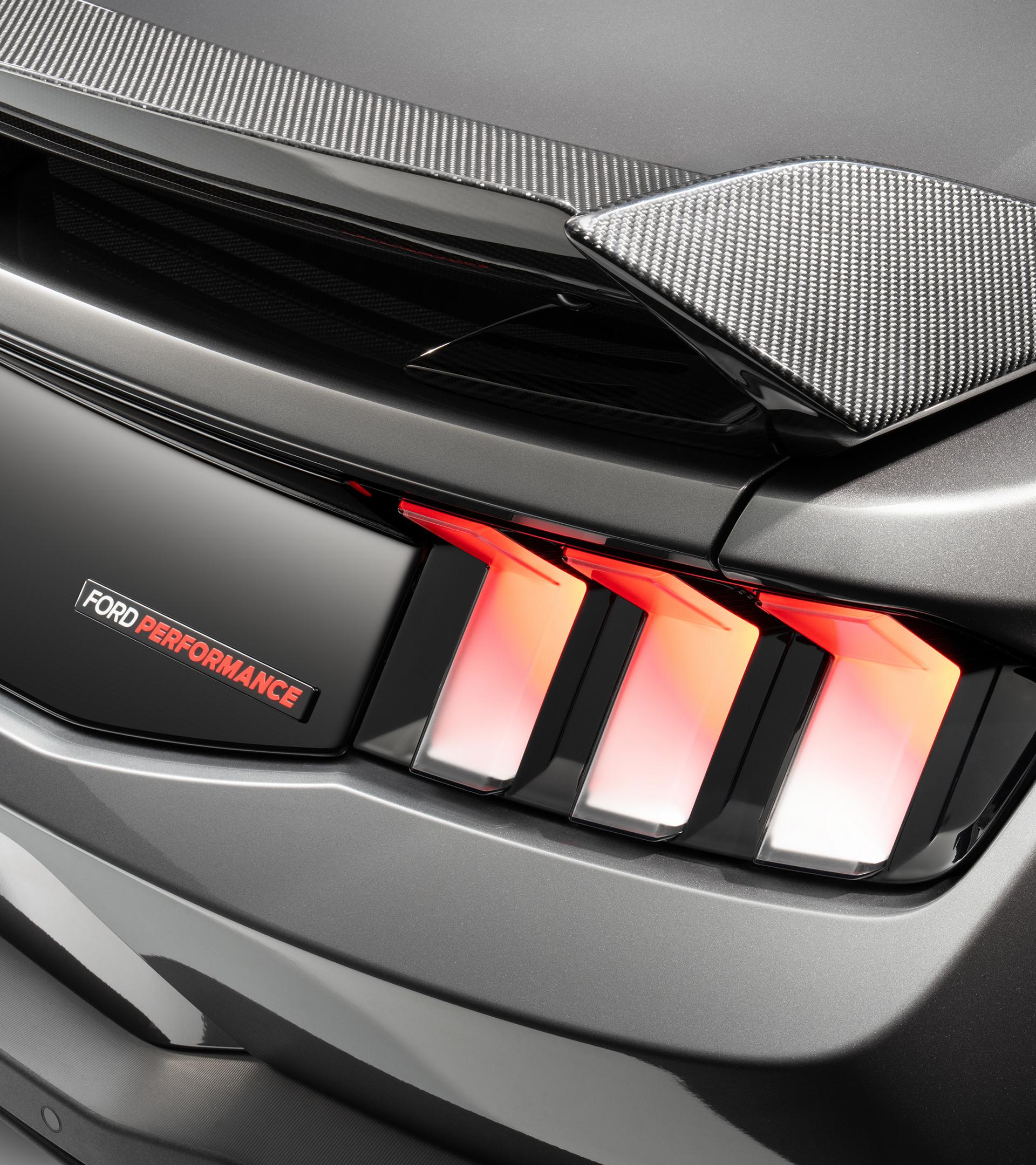 Rear detail of the gloss black trunk appliqué and Ford Performance badge beside the illuminated tri-bar taillight, under the carbon-look rear spoiler