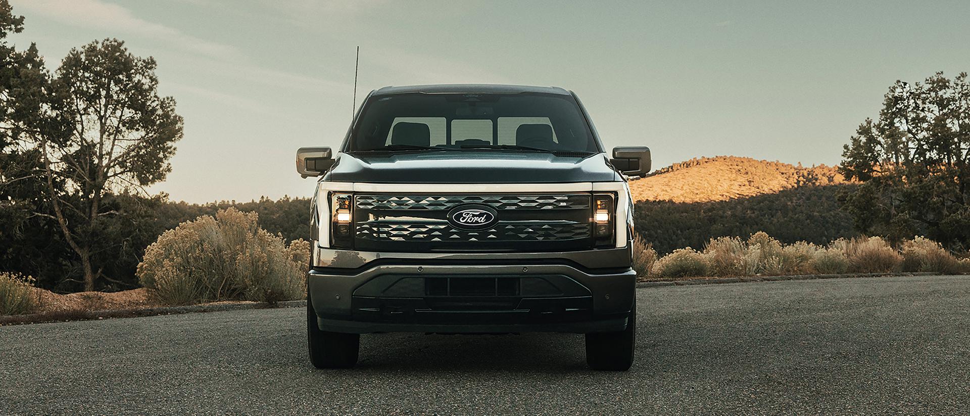 A 2025 Ford F-150® Lightning® in Carbonized Gray parked with a hilly terrain in the background