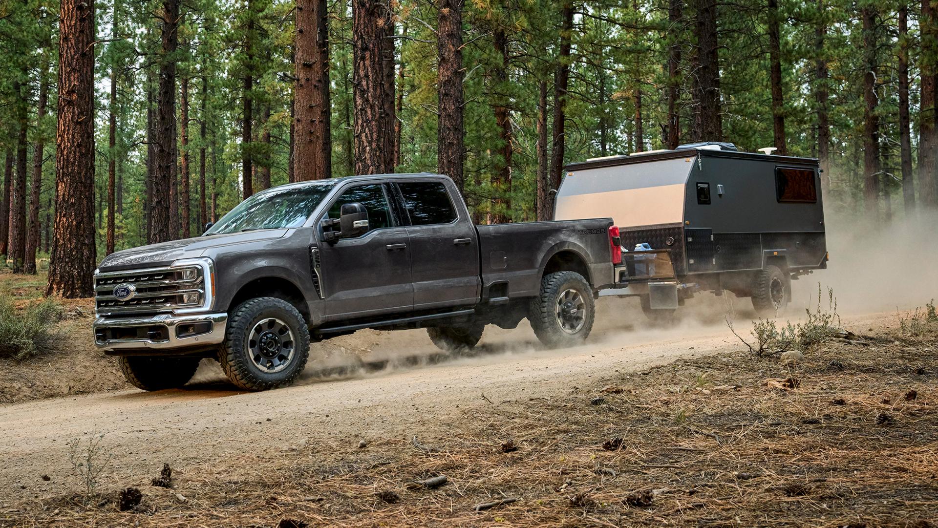 2027 Ford Super Duty® F-250® with the Tremor® Off-Road Package pulling a camper on a dirt road in the woods