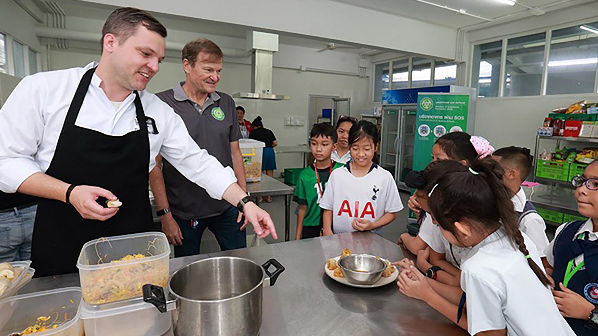 A chef draws the attention of a group of kids to an entrée being prepared