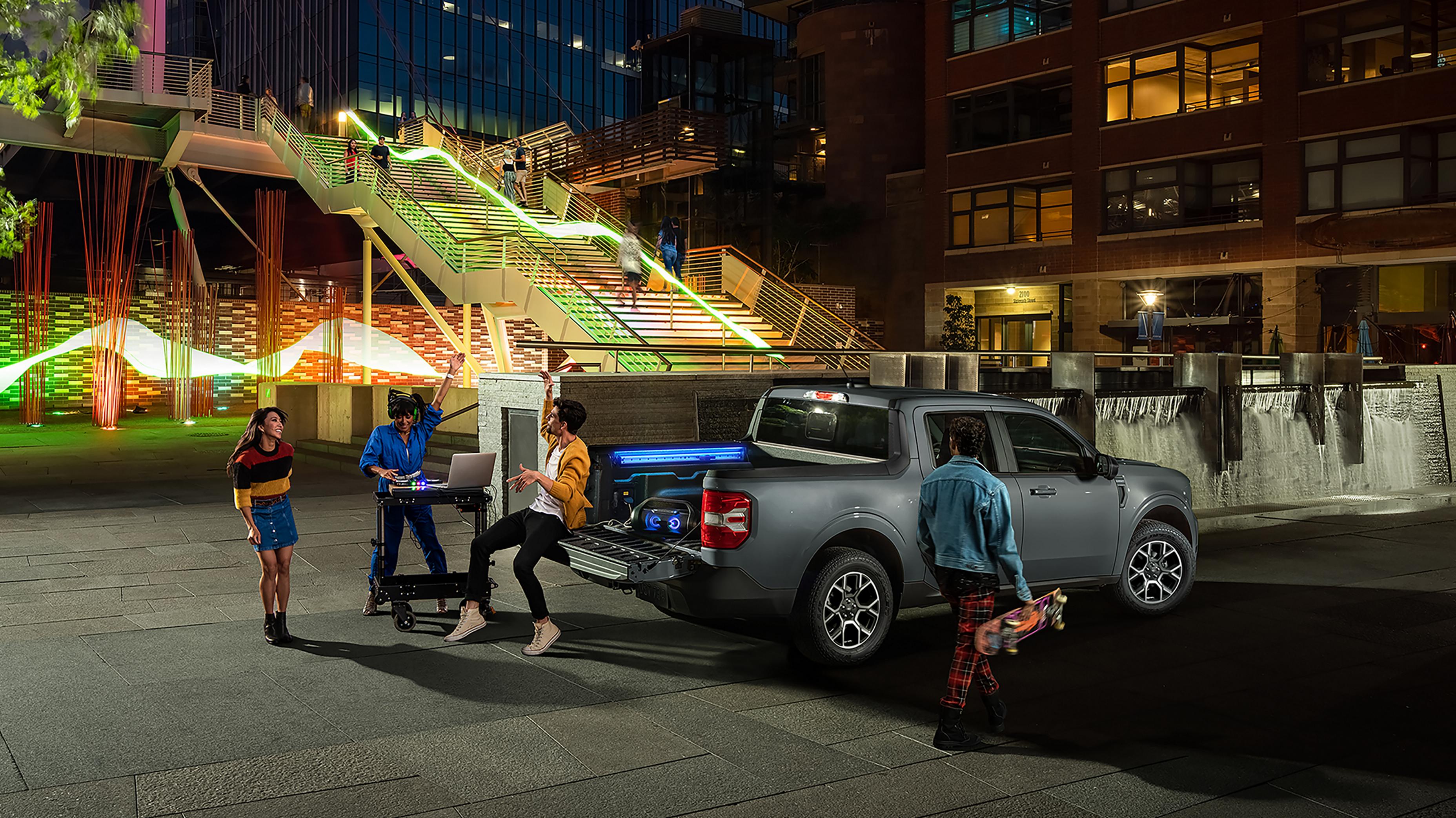 A group of people gathered near a 2026 Ford Maverick® pickup with DJ equipment plugged into the cargo bed outlet