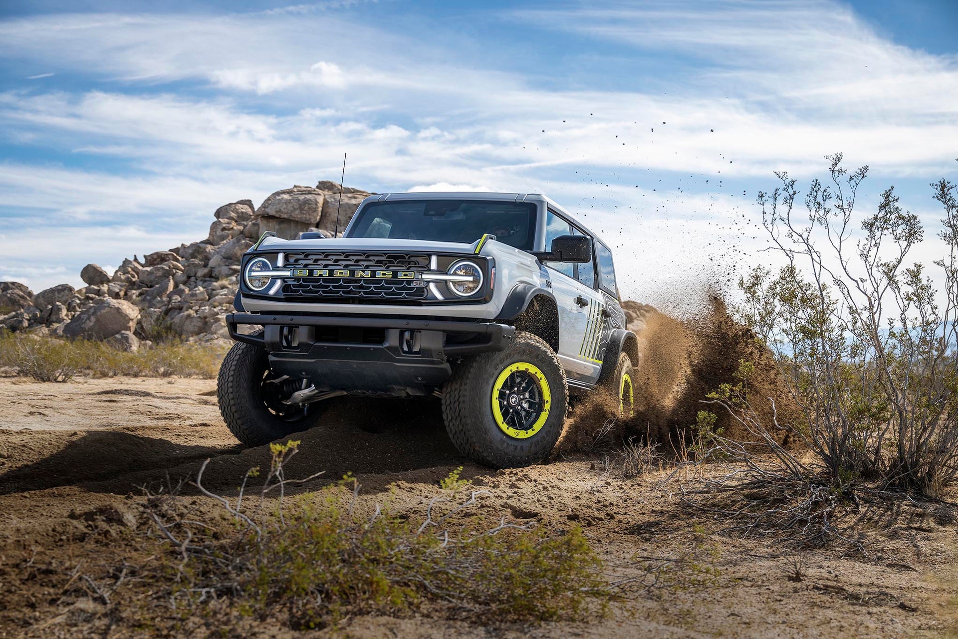 A white 2027 Ford Bronco RTR with Hyper Lime wheel accents driving through desert terrain