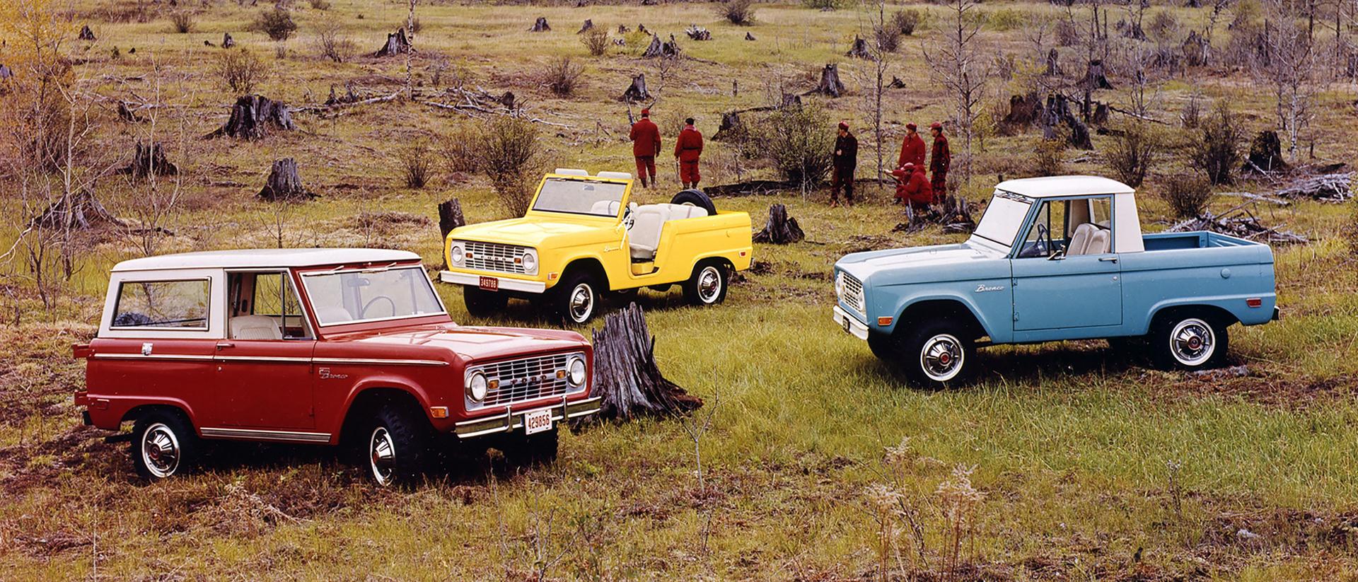 A family of vintage Ford Bronco® models parked amidst a cleared forest