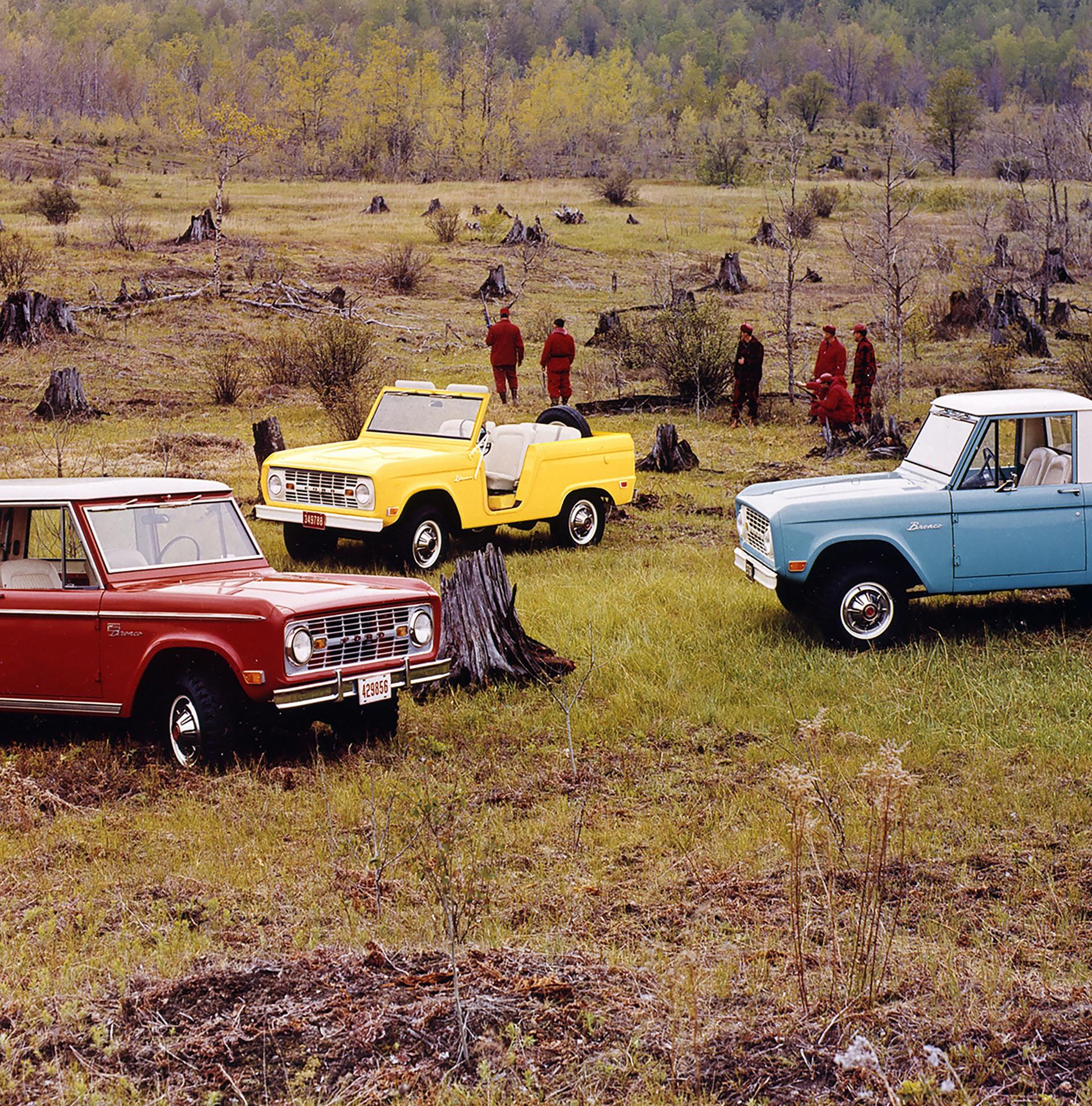 A family of vintage Ford Bronco® models parked amidst a cleared forest