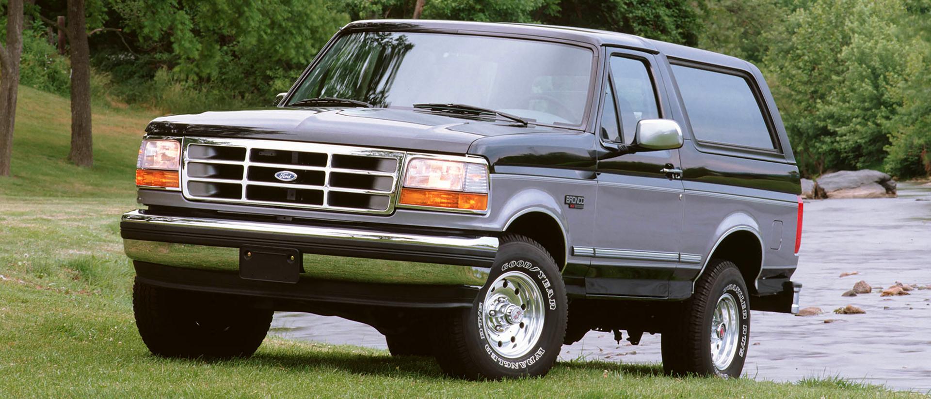 A two-tone gray 1995 Ford Bronco® model parked at a river's edge