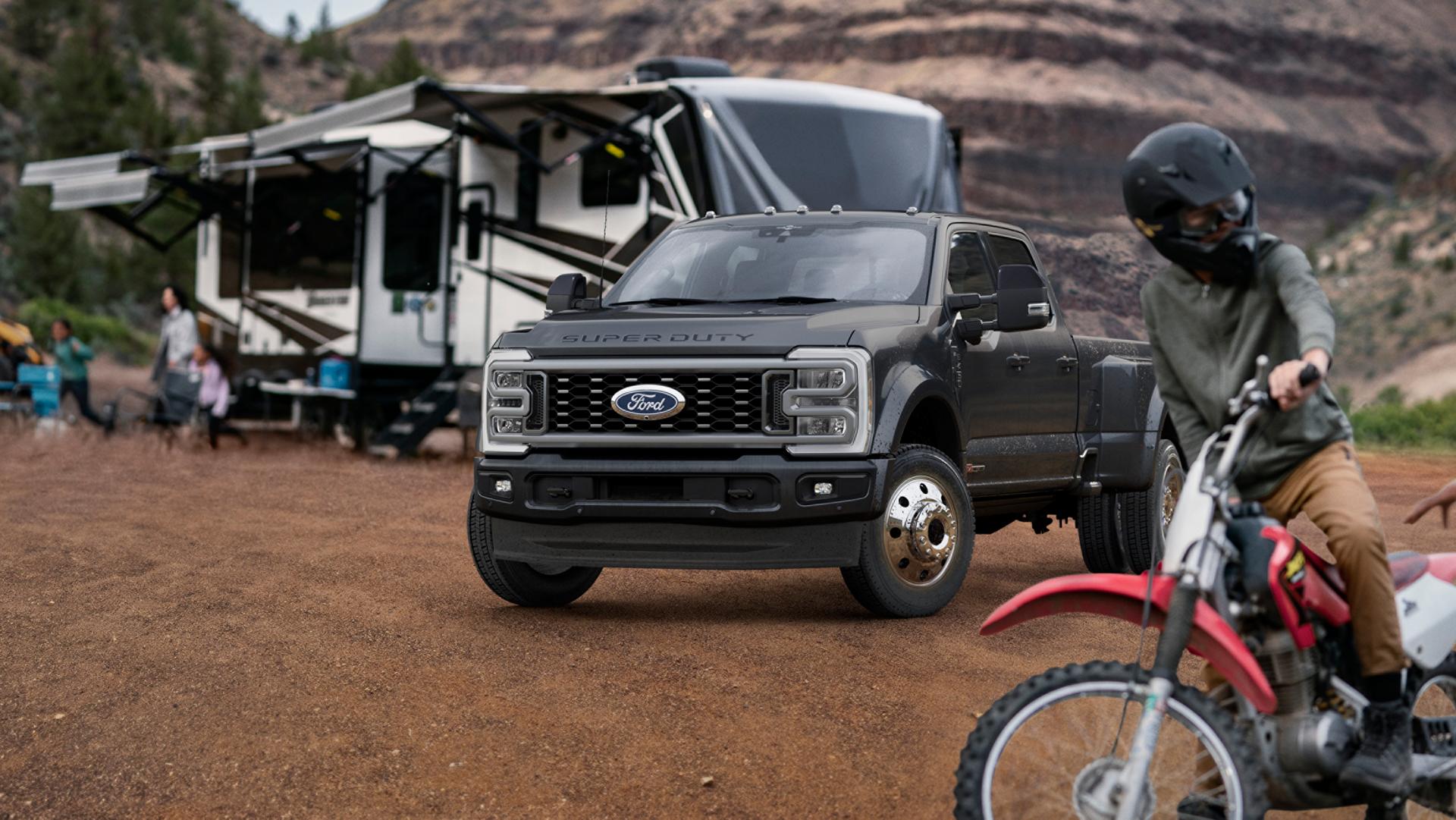 2027 Ford Super Duty® F-450® Platinum® model in Carbonized Gray parked on a campground with a camper in the background
